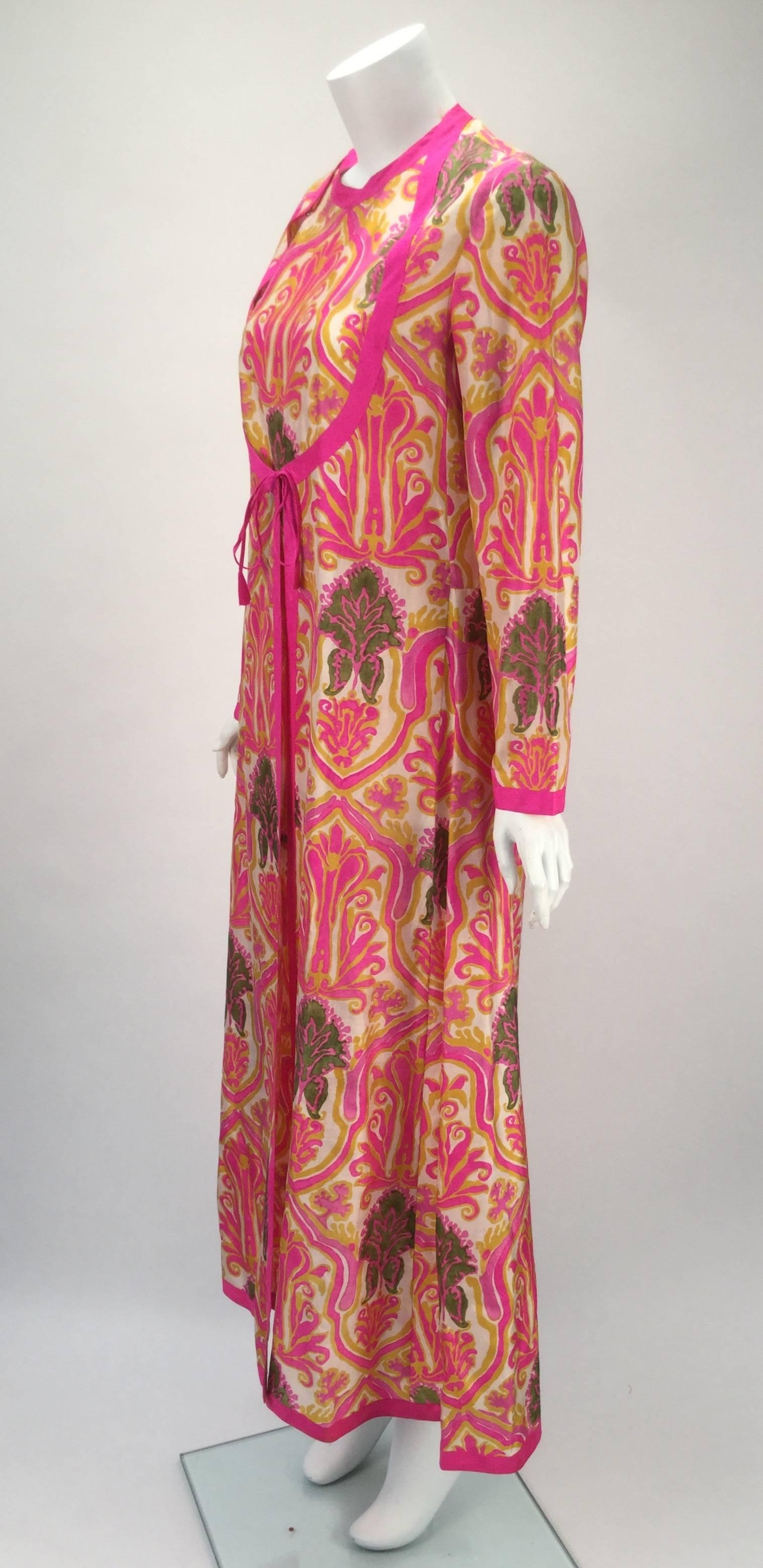 Absolutely gorgeous 1960's silk multi-color ethnic kaftan with long sleeves. The fabric is brightly colored fine silk with a hot pink trim. There are snaps that attach the bib style bodice down and around to center front. Hot pink edging ties at