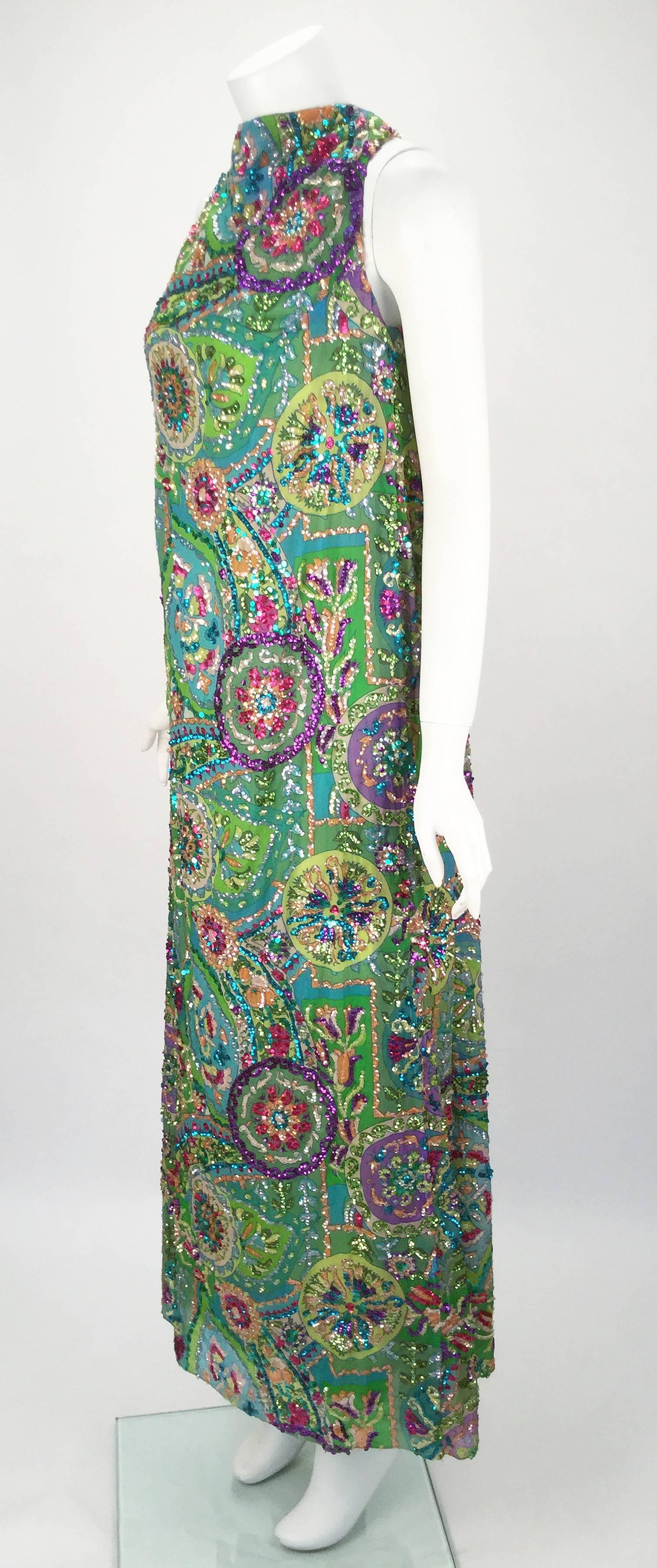 Absolutely fantastic heavily beaded maxi dress from Sara Fredericks. The dress is covered in jewel tone and iridescent sequins over an interesting print with several mandalas. Gathered from the high neck the dress falls like a waterfall of pleats to