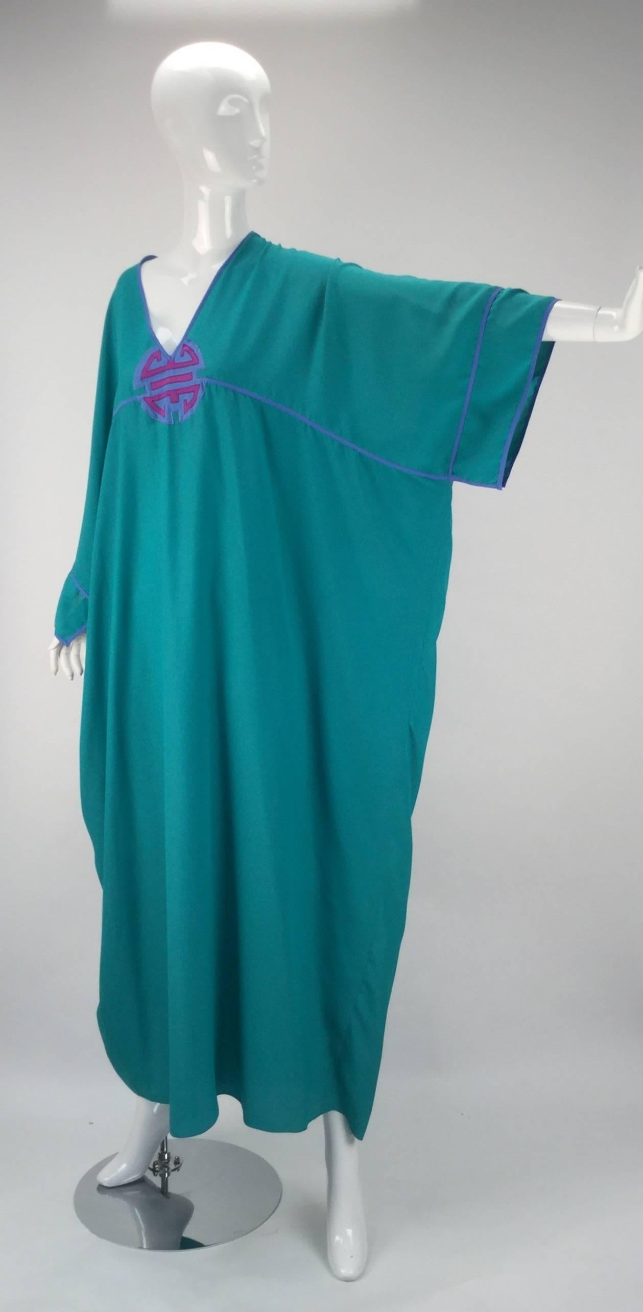 Enter into zen with this 1970s Bill Tice Asian medallion Kaftan. It features a V neckline with an embroidered Oriental medallion appliqué that rests at center front. Beautiful aqua colored light weight fabric. Dark periwinkle seam binding borders