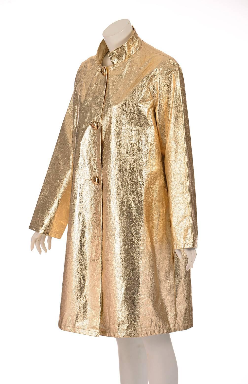 A late 1950s gold coat. This gold foil coat looks as though it were gilded! This fantastic coat is knee length and has three shiny gold buttons running down the front, as well as long sleeves, and a stylish high vintage collar. The interior of the