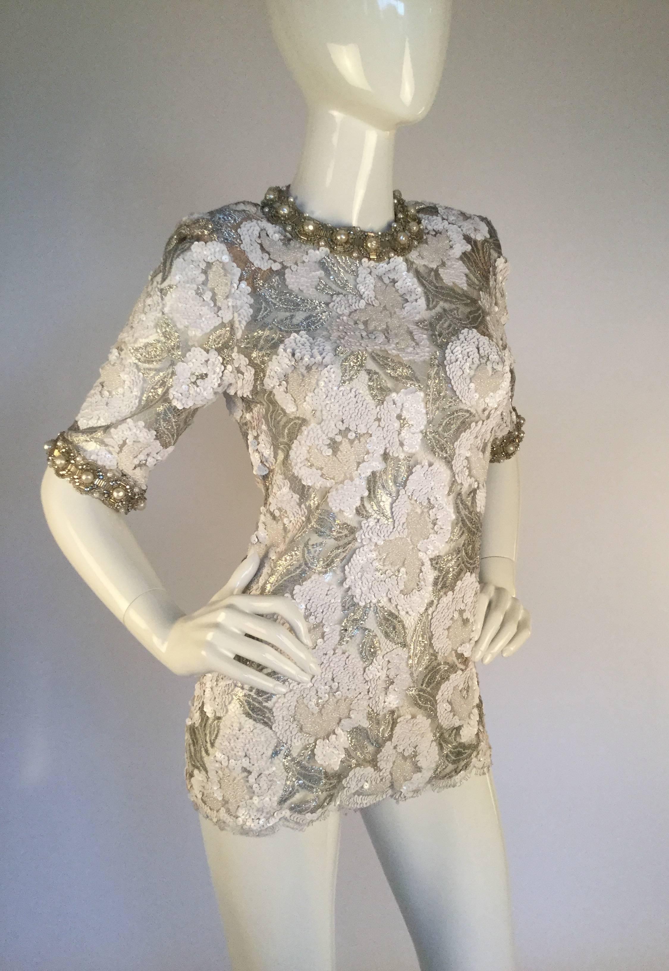 Simply devine 1970's silver semi sheer metallic lace top by Adolfo. Short sleeves with a scalloped edge compliment the top as it is finished with a gorgeous ivory circular pattern of pearls, clear rhinestones, and beading. The neckline is bordered
