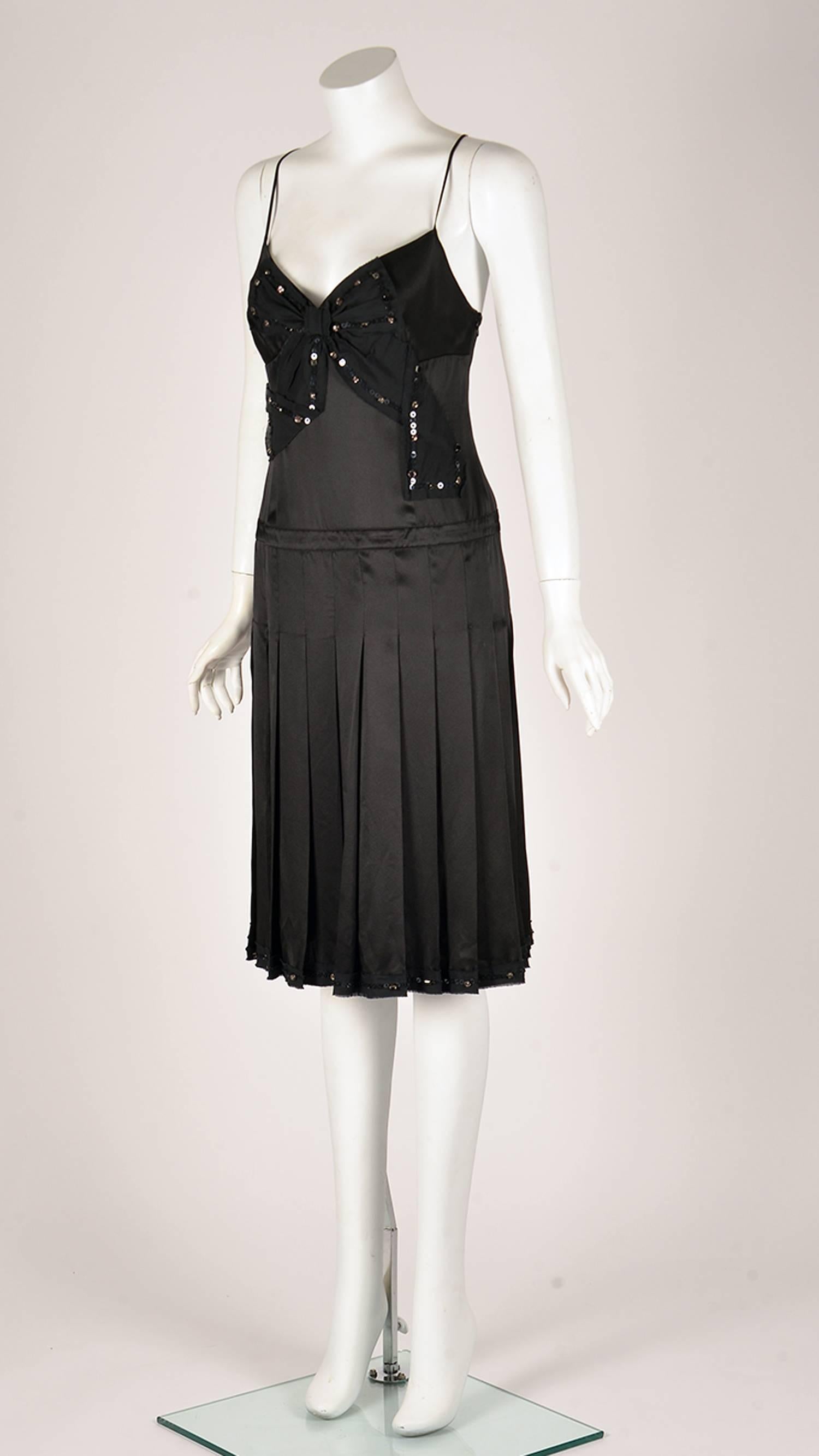 Moschino Cheap and Chic black silk spaghetti strap drop waist cocktail dress.  The dress has a black bow applique with sequin and clear rhinestone trim at center front, as well as a gently pleated skirt. The dress has a size zipper closure. 