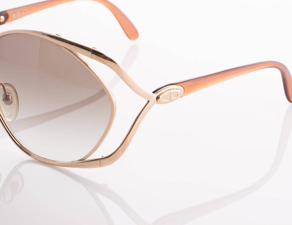 1980s Christian Dior Sunglasses. These modern, feminine sunglasses feature Dior's famous butterfly-design. The peach and gold-tone frames gently wrap around the oversized taupe gradient lenses. Frames have the Christian Dior logo on the side, over