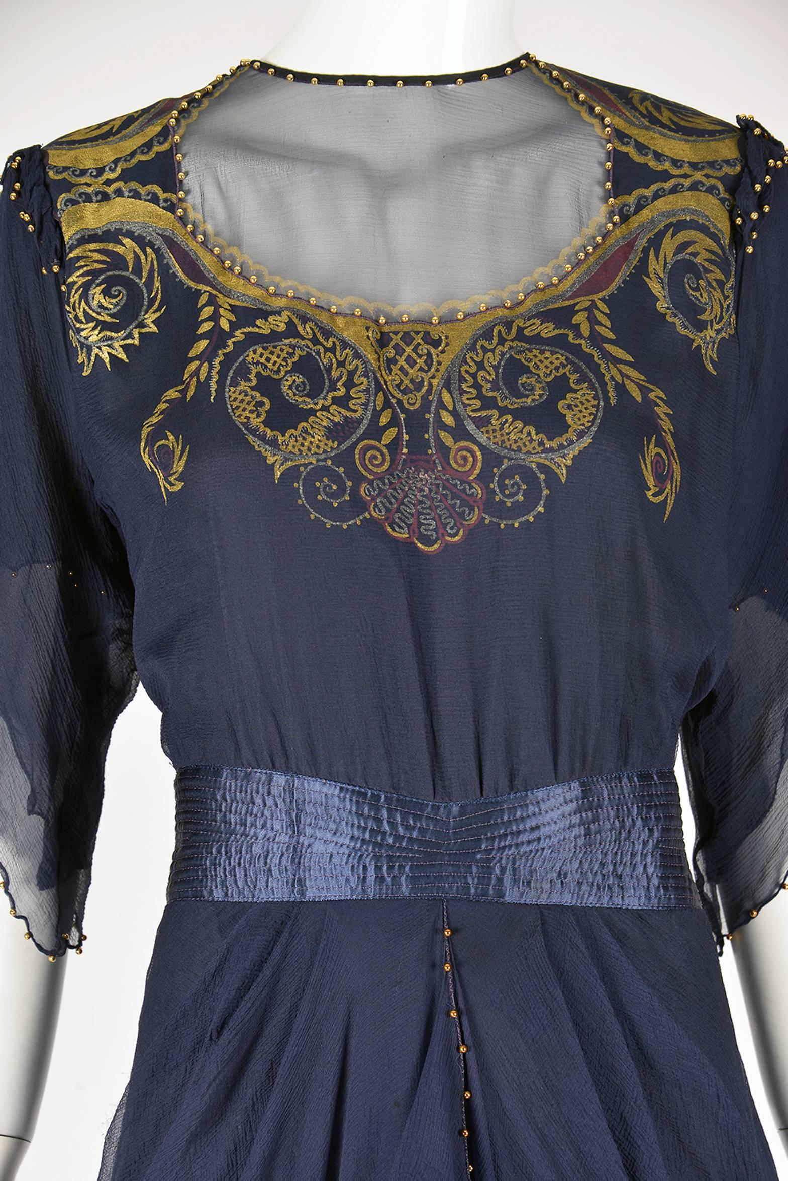 
Wonderfully designed & screen-printed 1970s Zandra Rhodes navy blue silk chiffon evening dress. Screen print is in gold around the neck and back. Small gold metal ball detail trim along the neck line and front yoke, continues on the