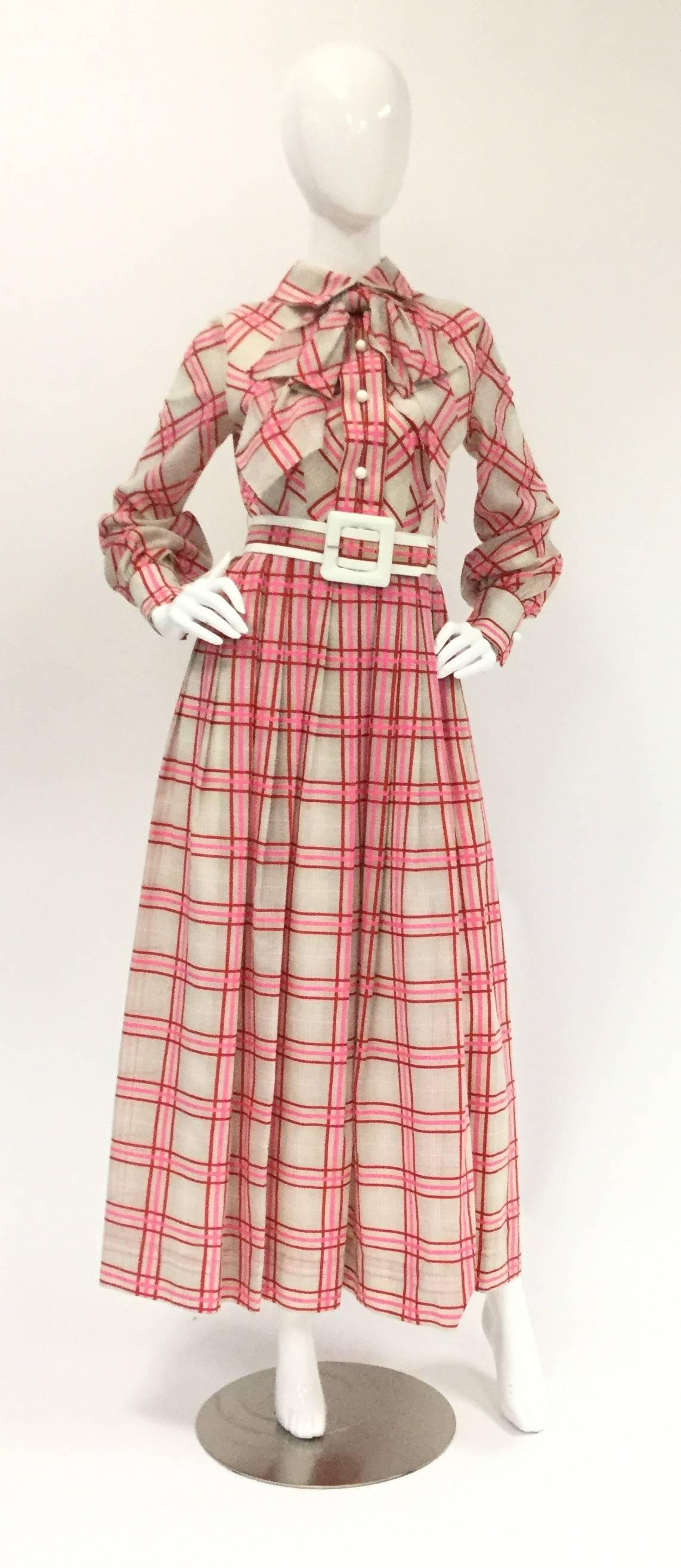
1970s Sweet and charming floor length dress by Victor Costa! This simple and cute dress features bishop sleeves with buttoned cuffs and a button-up bodice with collar and large dramatic neck bow. The ensemble includes a chunky plaid belt with white