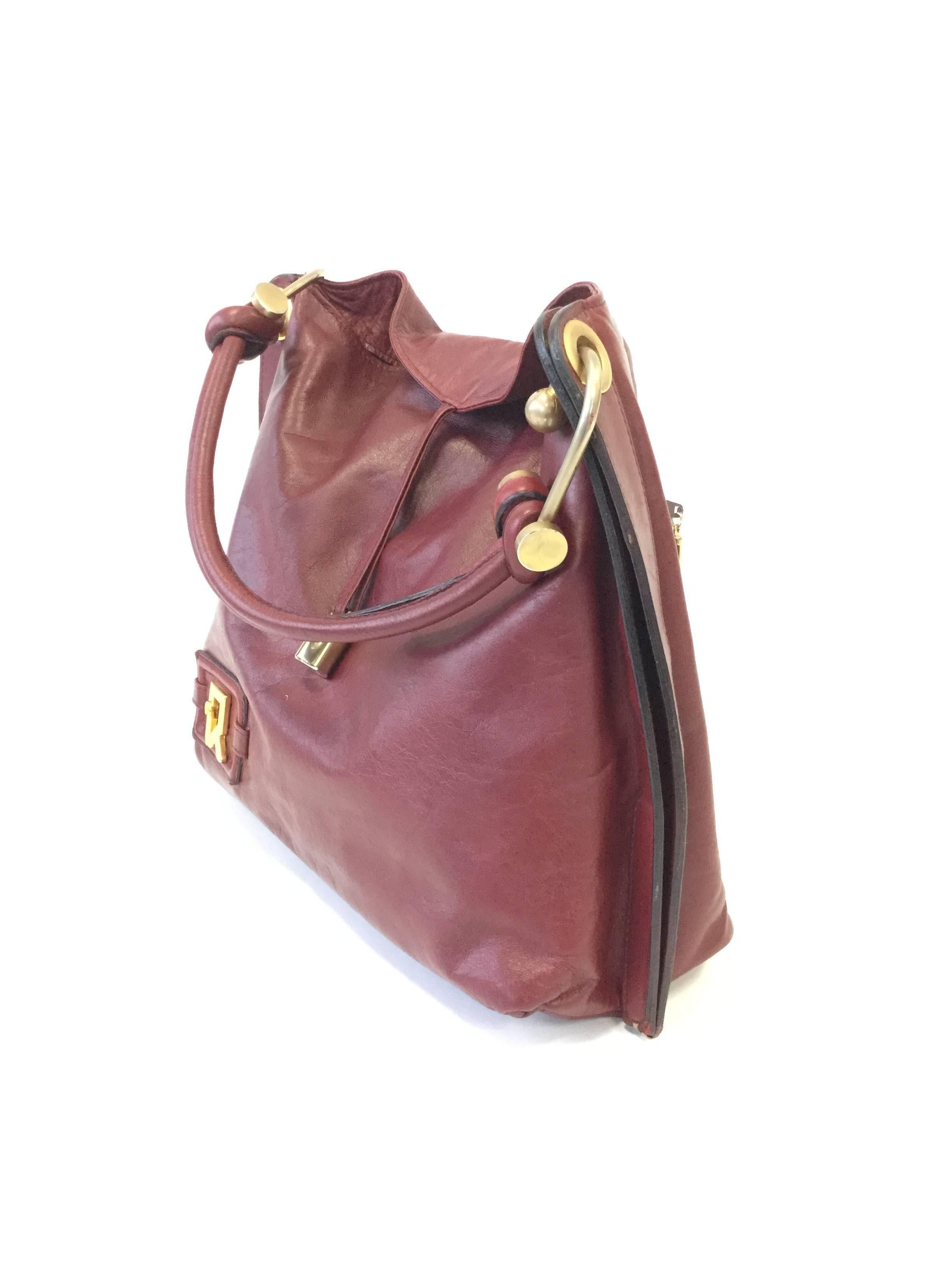 
Undeniably chic tote by Roberta di Camerino! This oxblood leather tote has a soft body stitched together leaving a thick section of leather at the side. The tote features a weighty lock-like piece of hardware suspended from a strand of leather;