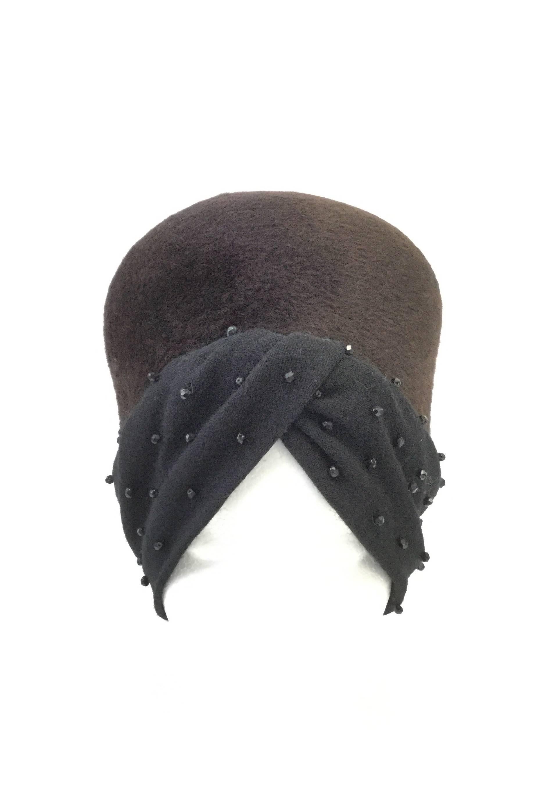 
Elegant and fun hat by Helios! This brown felt hat has a tall, rounded crown with a black beaded turban wrap base. The turban folds left over right and features medium-sized multifaceted black beads, adding a fun little sparkle to the elegant hat.