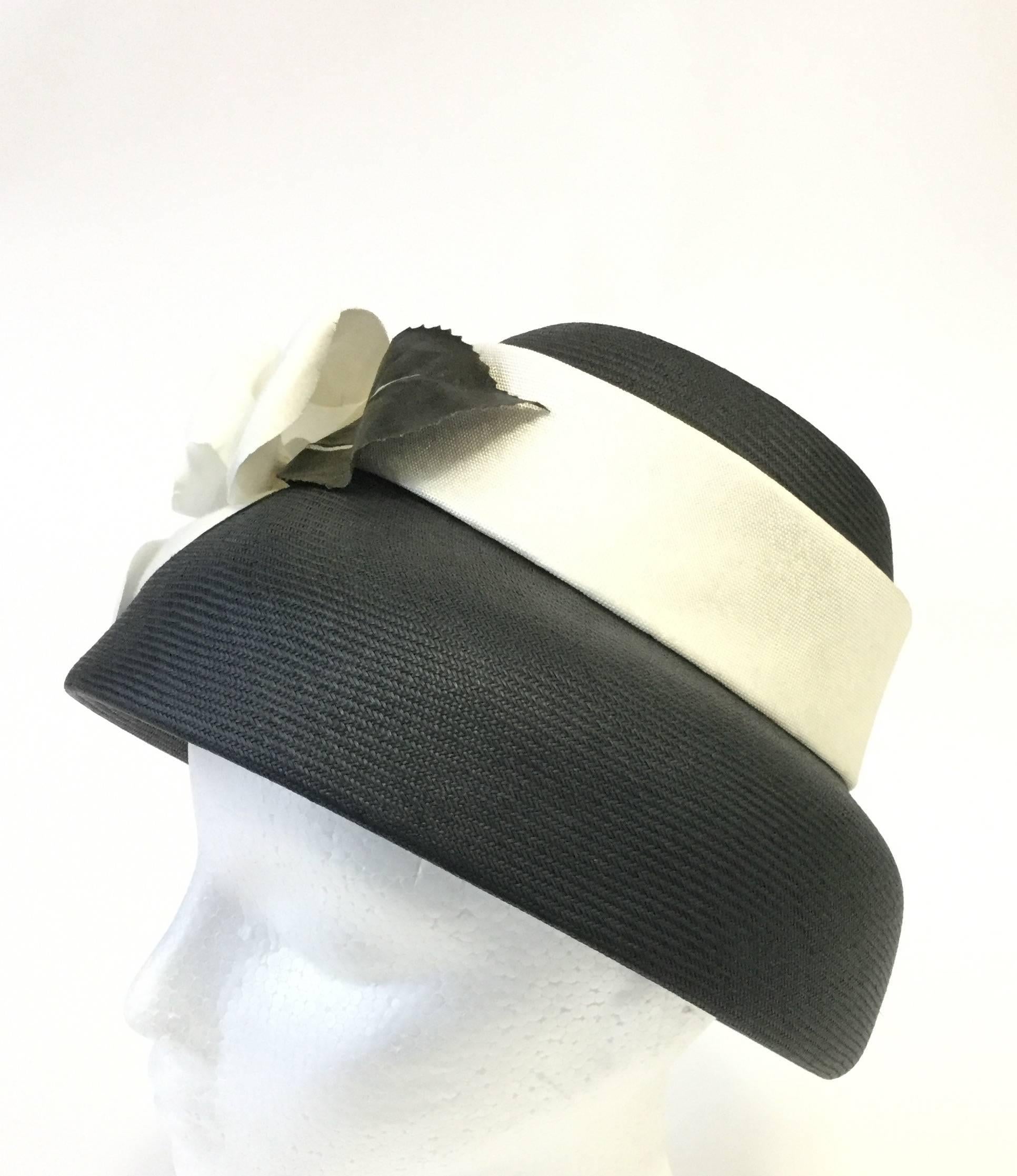 
Sweet and elegant hat by Jan Leslie! This classic hat by Jan Leslie is composed of a black woven mushroom style base with a striking white ribbon wrapped around the crown. Affixed to the ribbon is a large, white magnolia flower with dark leaves.