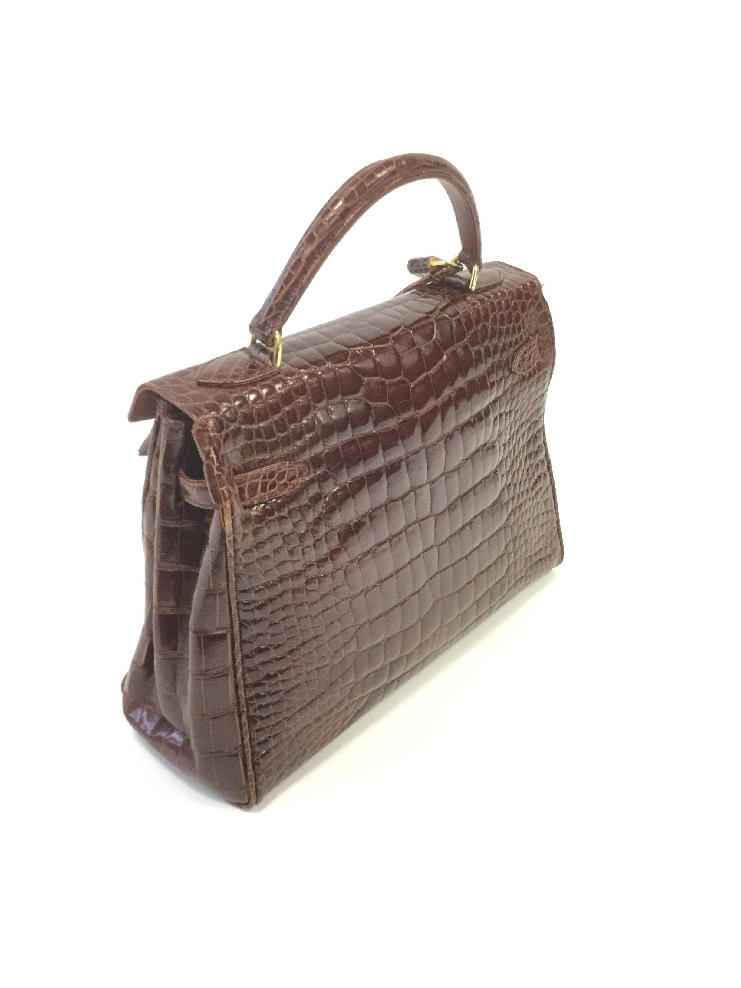 
This gorgeous chocolate brown alligator skin handbag by Revillon is an absolute dream! The purse is composed of a rectangular body with accordion side folds kept in place by two leather straps that meet in the middle and loop through the locking
