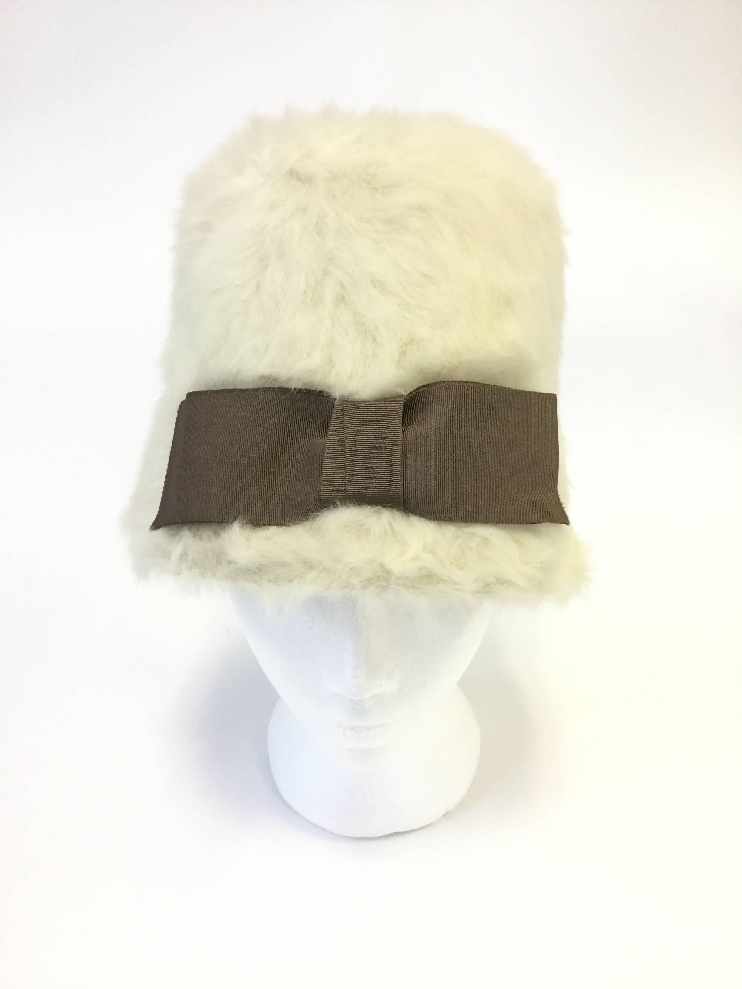 
Fantastic hat by Miss Dior. This fantastic Miss Dior hat by Christian Dior has an elongated cloche shape with a long crown and small, sloping brim. The hat has a soft white, plush, brushed cropped angora exterior, with a large olive accent bow. The