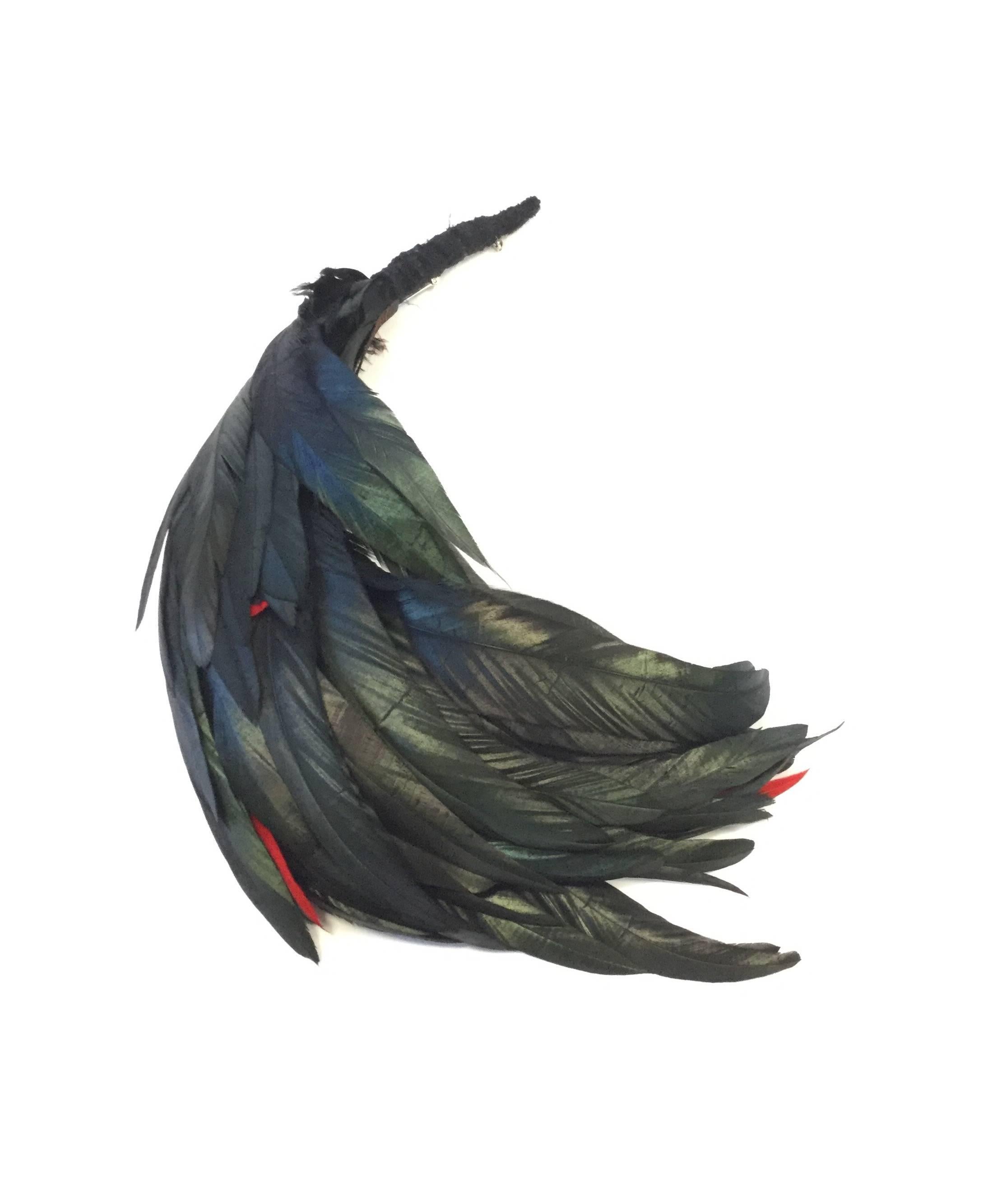 
Absolutely dramatic and versatile! This coque tail brooch by Yves Saint Laurent is composed of multiple long iridescent feathers that gleam green, blue, and gold. The occasional bright red feather can be seen peeking out from in between the waves