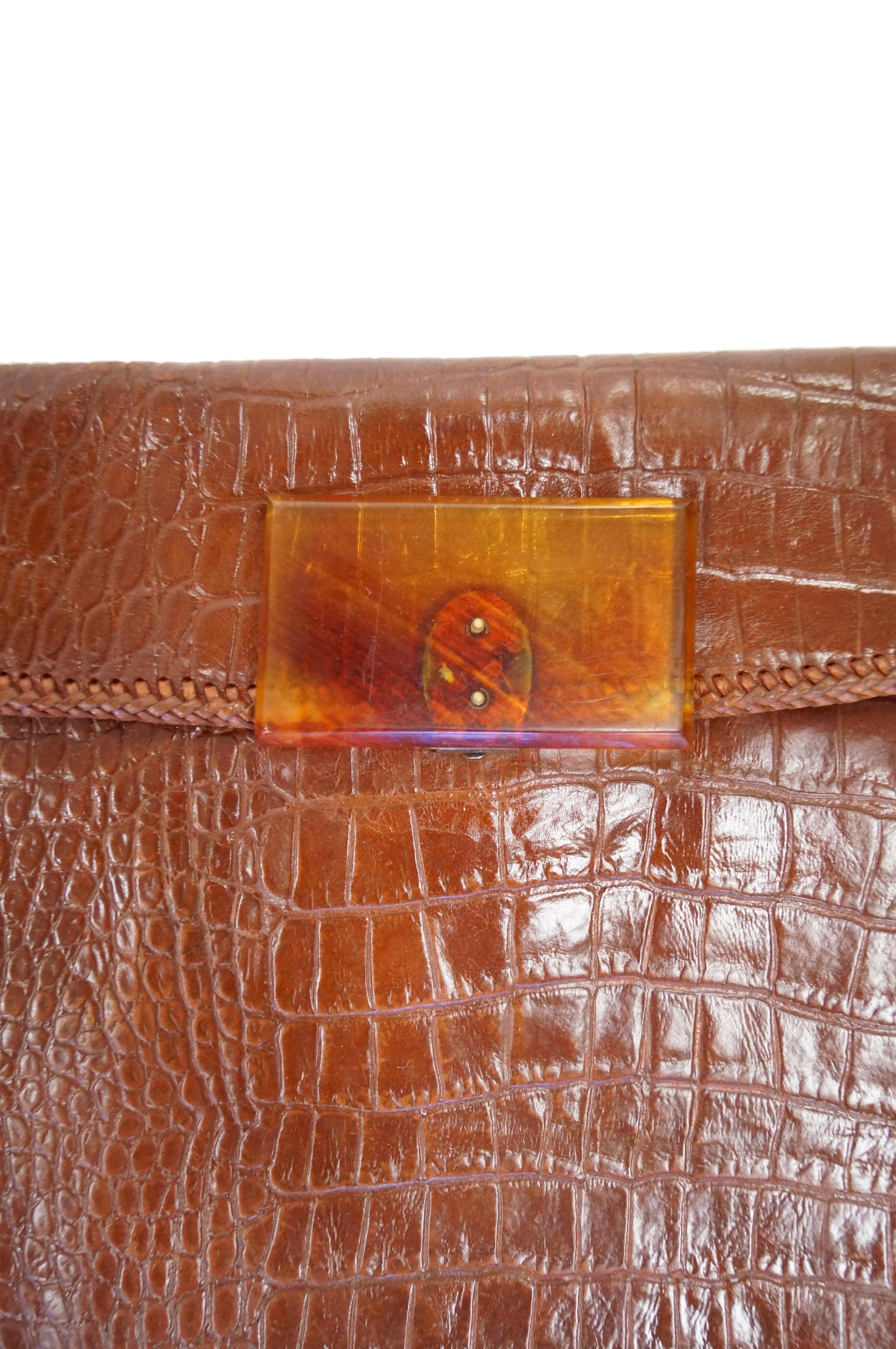 Amazing glossy chestnut brown alligator clutch! This clutch has a trapezoid - like rectangular silhouette, with a protruding flap. The edges of the alligator skin are held together by braided stitching. Lucite clasp. 

