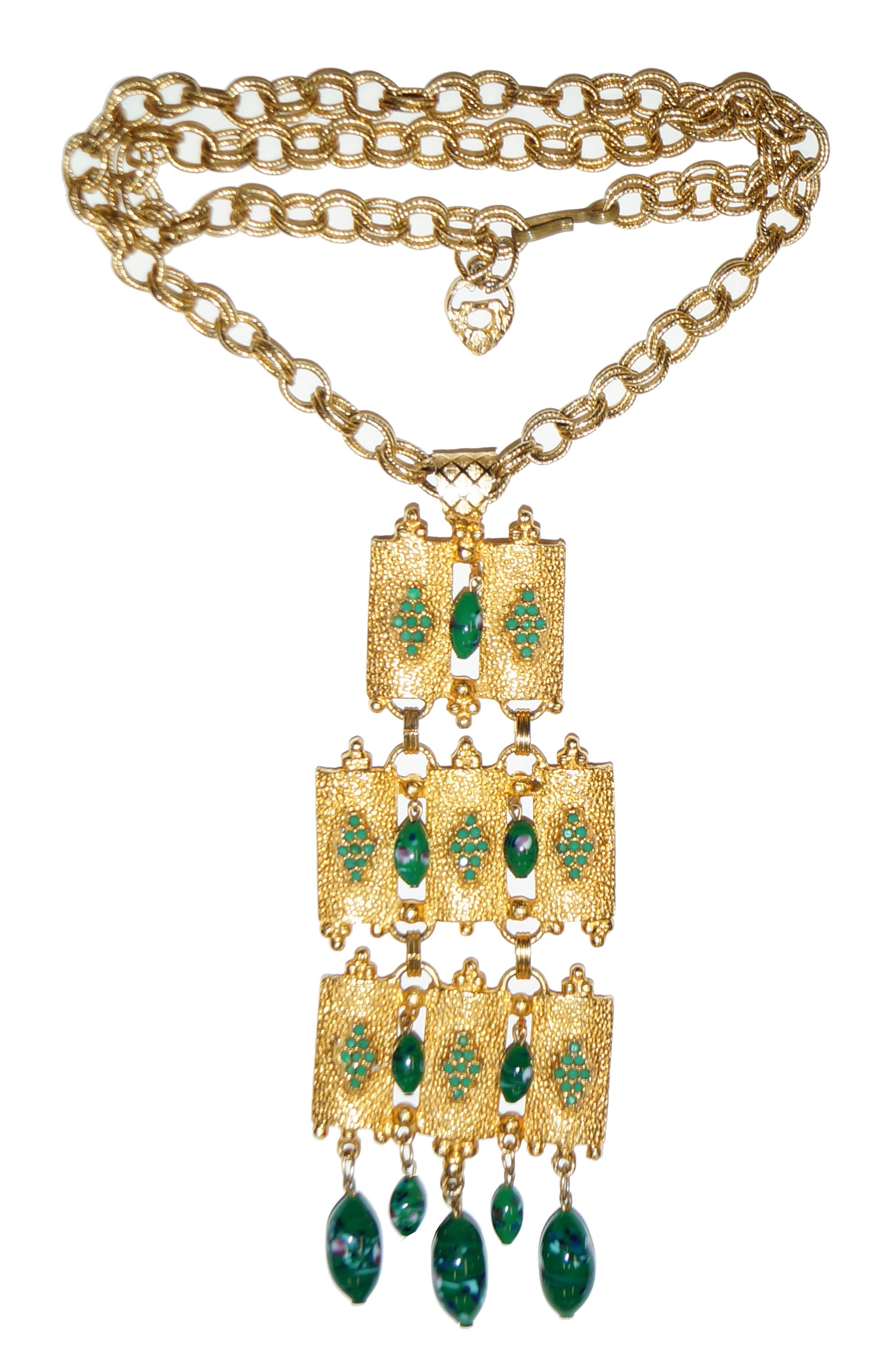 Large scale brutalist pendant hangs from long gold chain made of double rings. Pendant has green poured glass dangling beads and opaque green rhinestones inlaid in a diamond pattern. Three sections are connected with gold loops enabling movement.