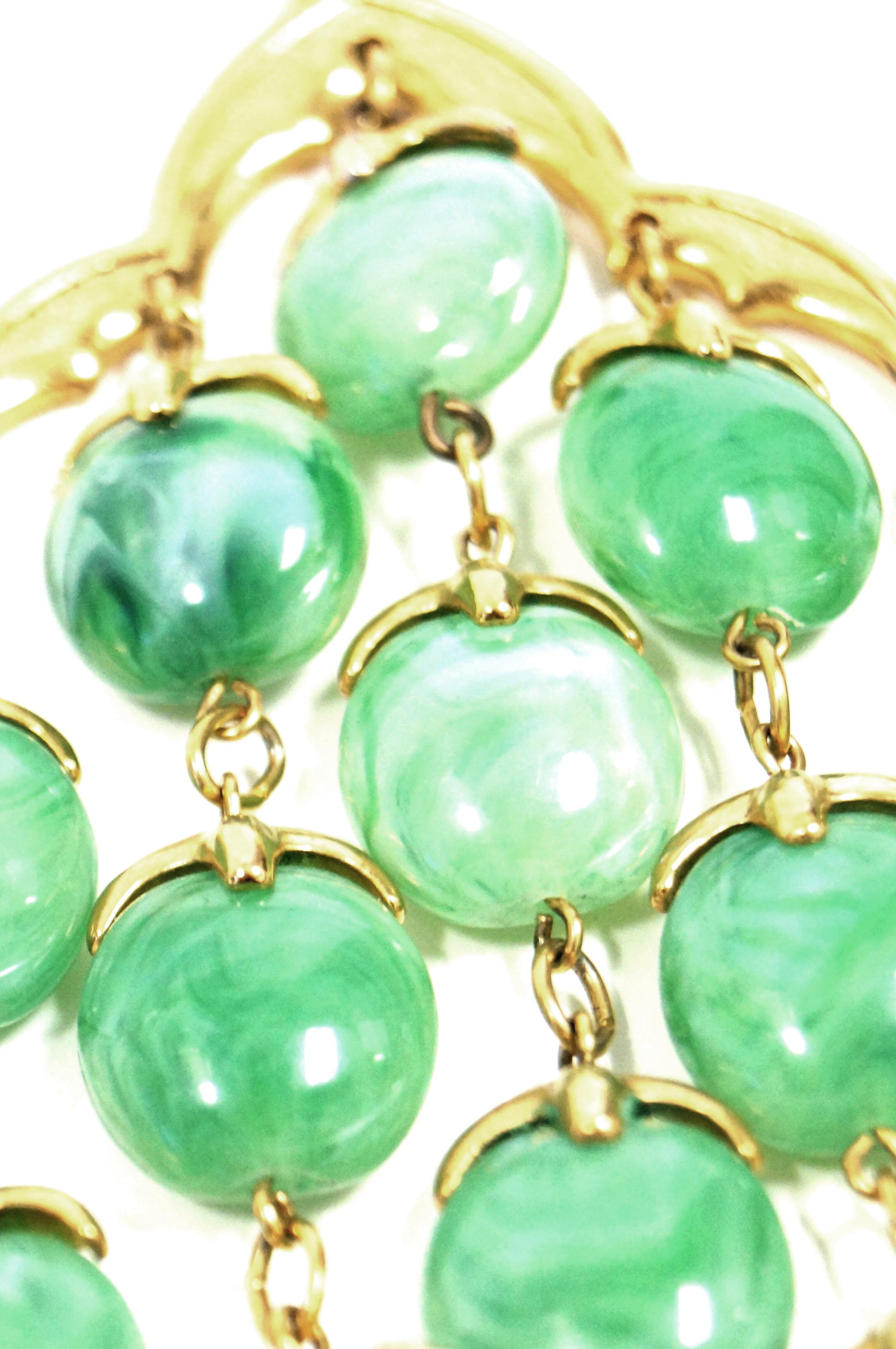 Gold tone long snake chain swings with this late 1960s Trifari pendant. Pendant has gold tone bails that hold a waterfall of green lucite beads. This statement necklace stands alone and is the perfect accessory for your look.

Trifari was founded by