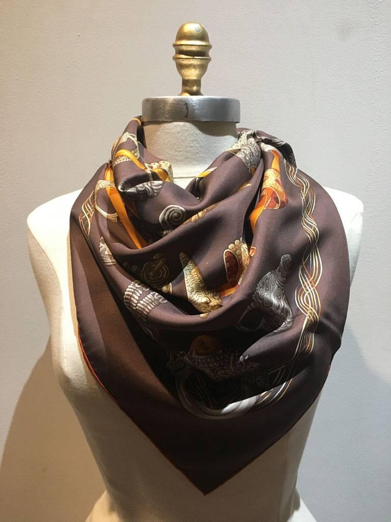 BEAUTIFUL Hermes alliances du monde silk scarf in excellent condition.  Original silk screen c2004 design by Annie Faivre features a neutral brown background with various grey, gold, and bronze rings woven through an orange ribbon and surrounded by