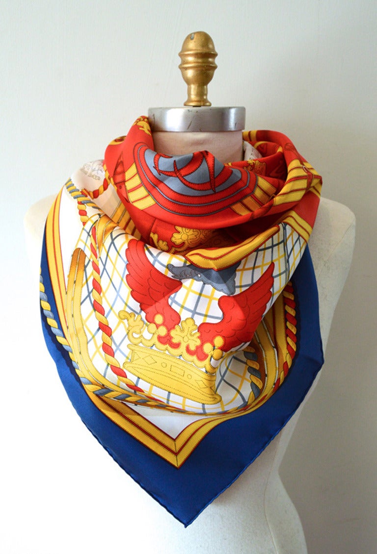 AUTHENTIC HERMES Vintage Grande Tenue silk scarf in excellent condition.  Original silk screen design by Henri d'Origny c1985 features ropes, ribbons, crowns, in red and golds surrounded by a navy blue border.  100% silk. Hand rolled hem. Made in