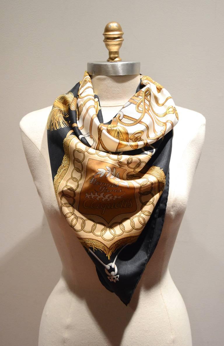 Wunderschöner HERMES Vintage Cliquetis Seidenschal in ausgezeichnetem Zustand.  Das originale Siebdruckdesign von Julia Abadie aus den 1970er Jahren zeigt verschiedene Schwert- und Quastenoberteile in verschiedenen Goldtönen auf einem schwarz-weißen