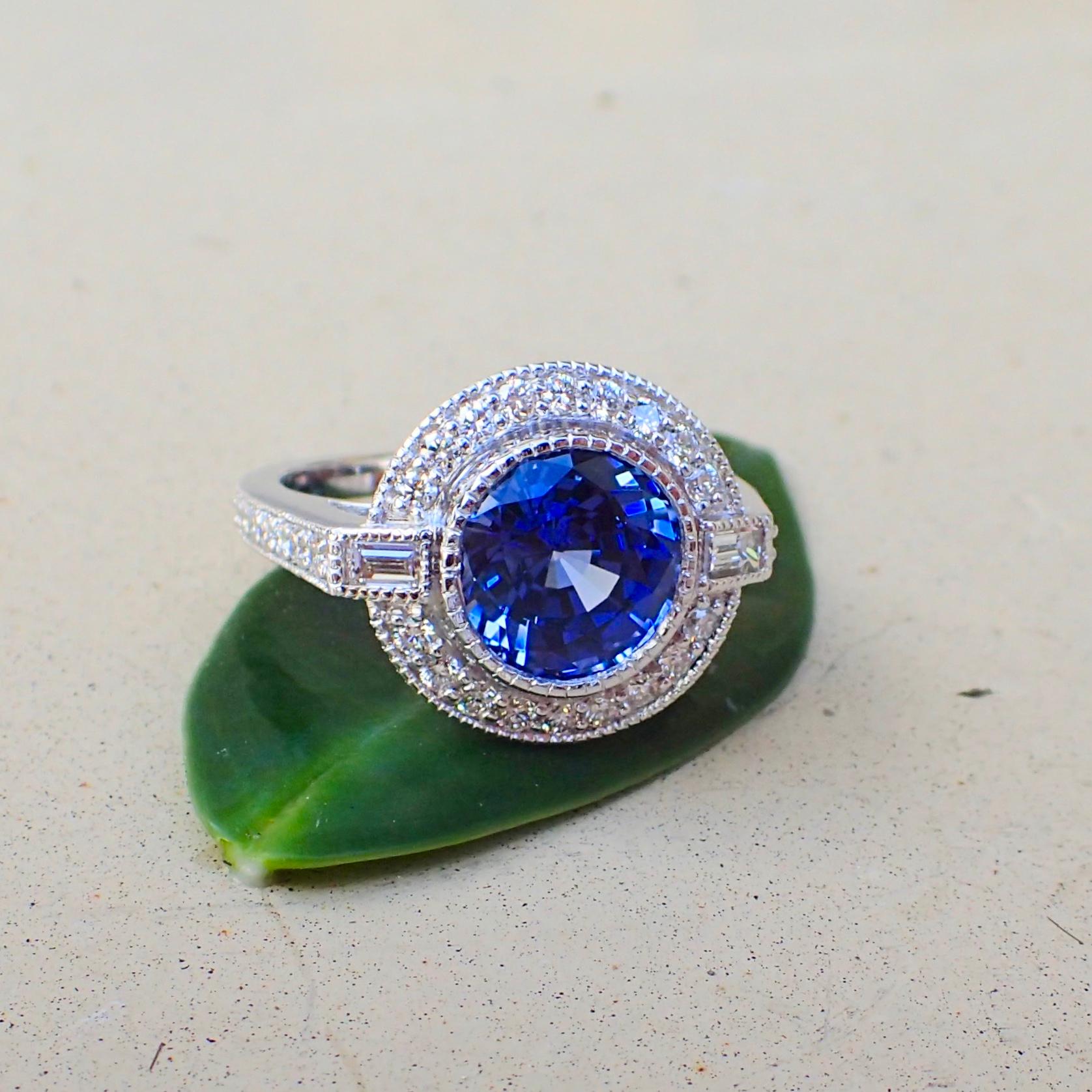 An 18k white gold ring is set with one (1) Round Brilliant Cut Chatham-Created Sapphire that measures 9mm x 9mm and weighs 3.93 carats with Clarity Grade VS-VVS and two (2) Baguette Cut Diamonds that measure 2.9mm x 1.9mm and 2.9mm x 1.9mm and weigh