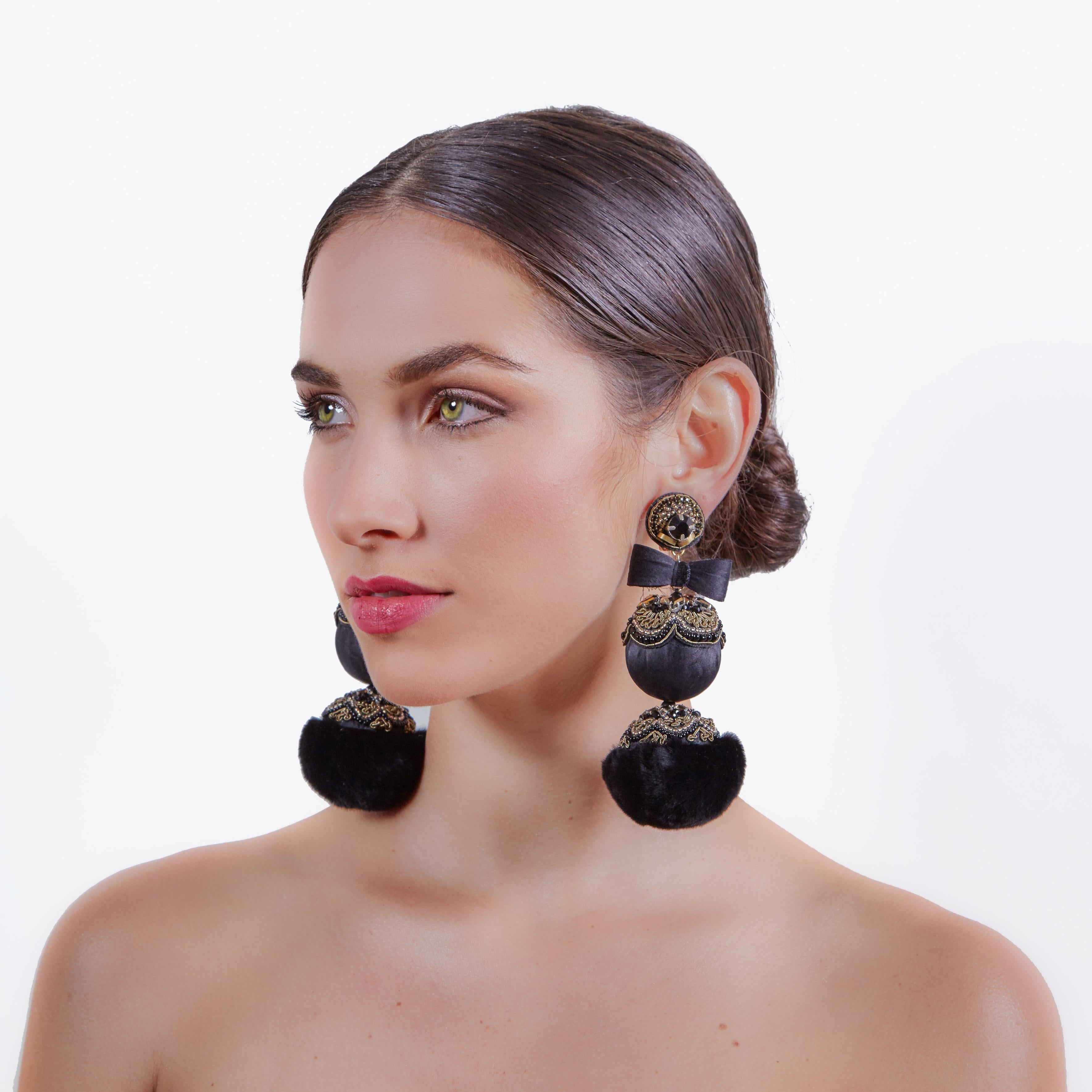 Add an element of dark elegance to your look with the Arpoador earring. Luxurious mink fur pompoms, satin bows, and crystals create an unparalleled level of sophistication.
