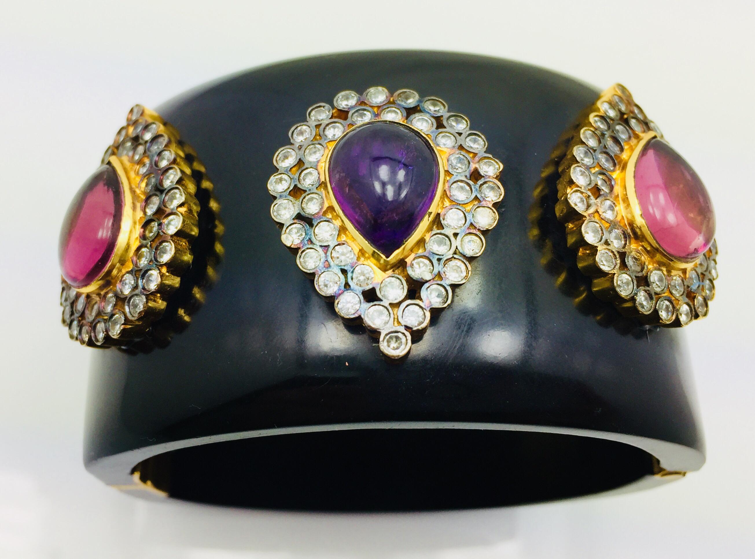 La manchette en résine Taj est fabriquée à la main avec trois fausses pierres d'améthyste en forme de poire.  Cette pièce audacieuse est entourée de  Zircons cubiques sur chaque motif inspiré du magnifique Taj Mahal. Le bracelet est articulé et se