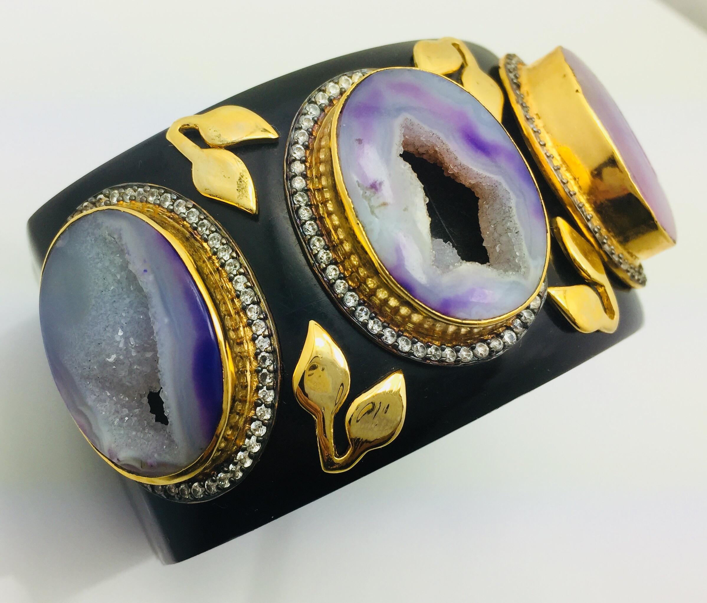 The smooth black resin bracelet provides a stunning backdrop for the one of a kind crater purple druzy stones. Each of the druzy is framed with dazzling cubic zircon and embellished with handcrafted leaf motif.  The bracelet is hinged and fastens