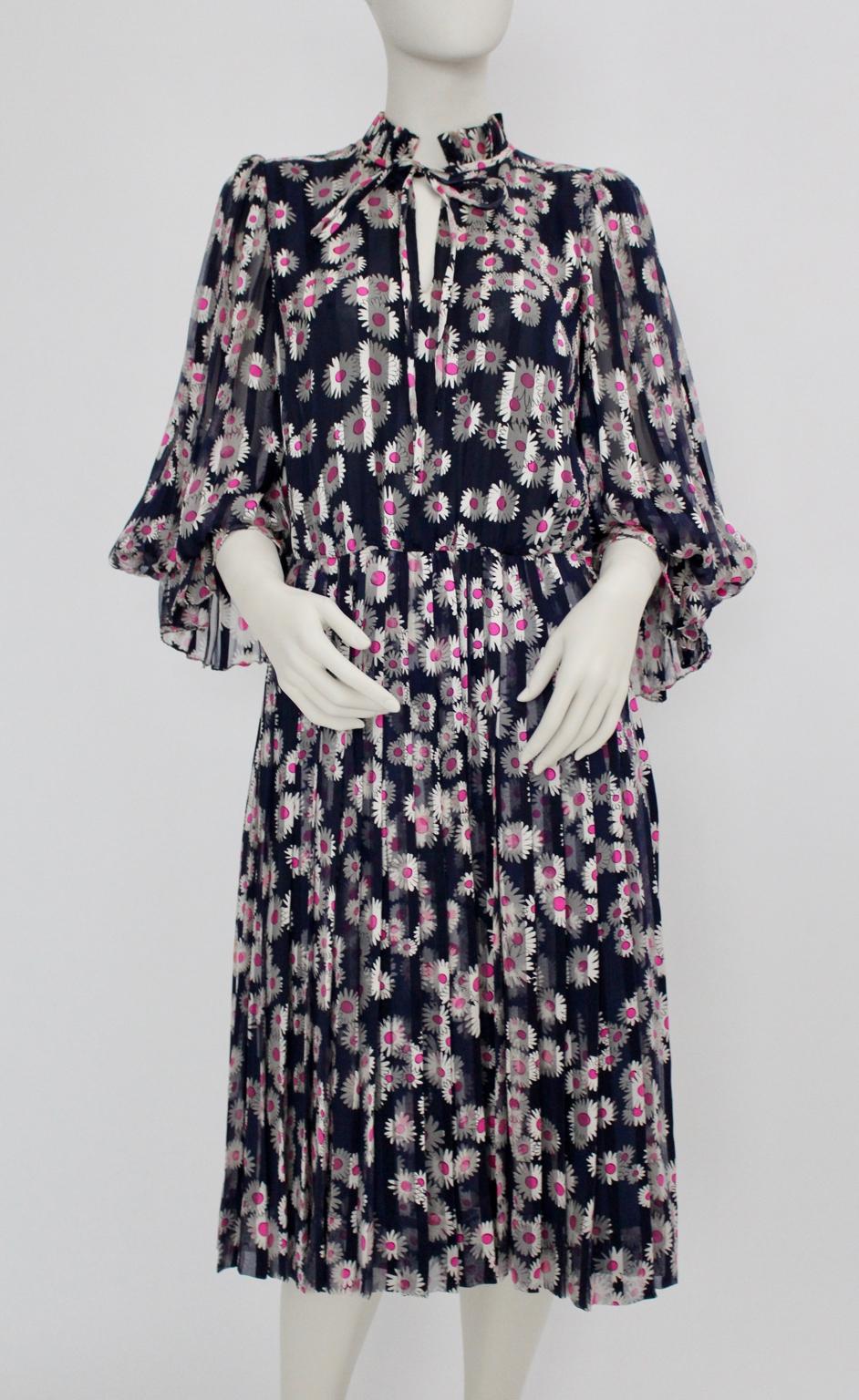 This vintage pleated Day Dress was designed and made in the early 1980s. The day dress impresses through the blue color and the pink daisies.
Also the skirt features pleats and is underlined. The upper part shows a standing collar, long sleeves with