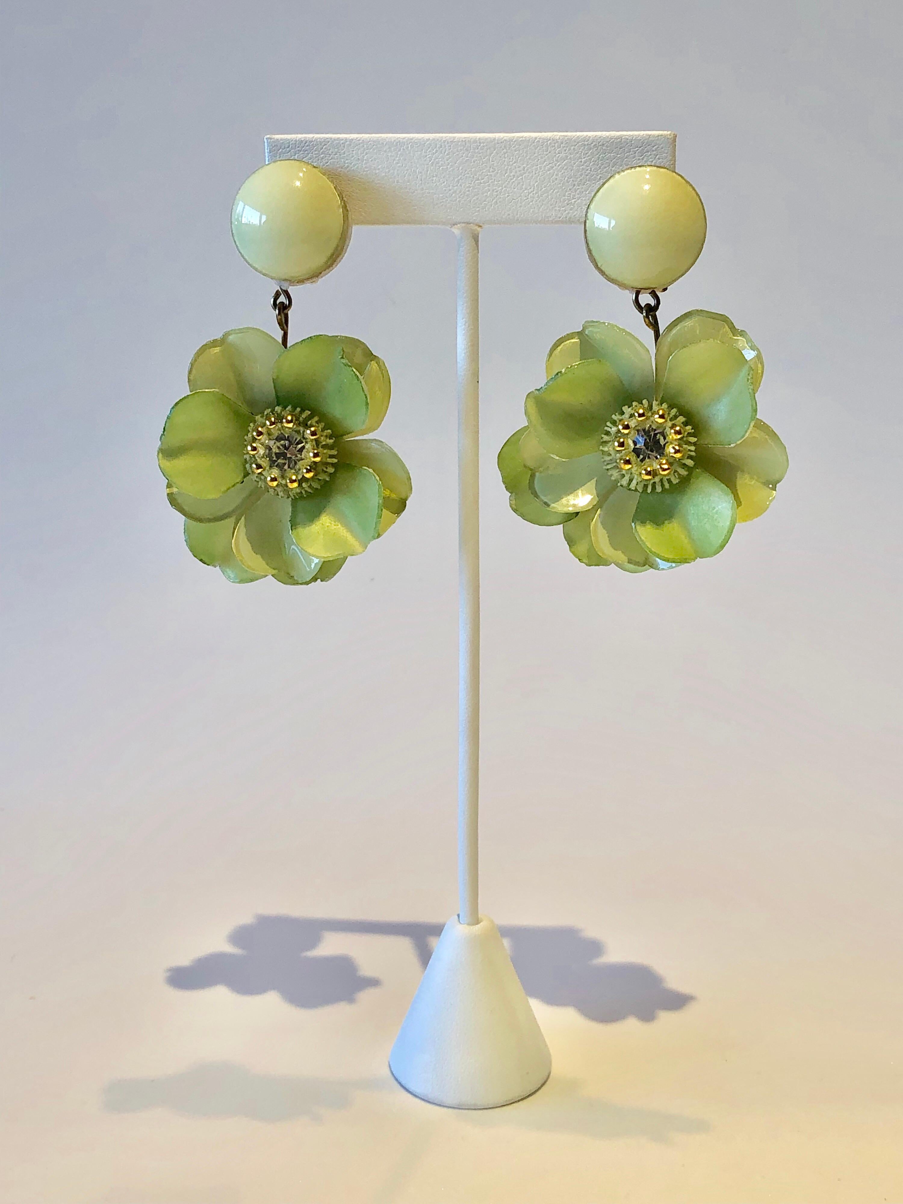Three-dimensional artisanal flower clip-on earrings by Cilea Paris. The enamel/resin earrings feature large pale green flowers which are accented by an elaborate detailed talosel center with a different pattern and a large clear rhinestone, giving