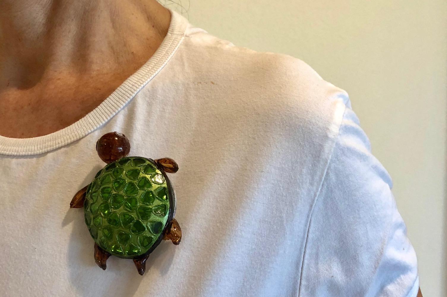 Light and easy to wear, this handmade artisanal pin was made in Paris by Cilea.  The lightweight pin features a single swimming turtle, comprised out of enamel and resin composite). The turtle's three-dimensional oversized body features bright