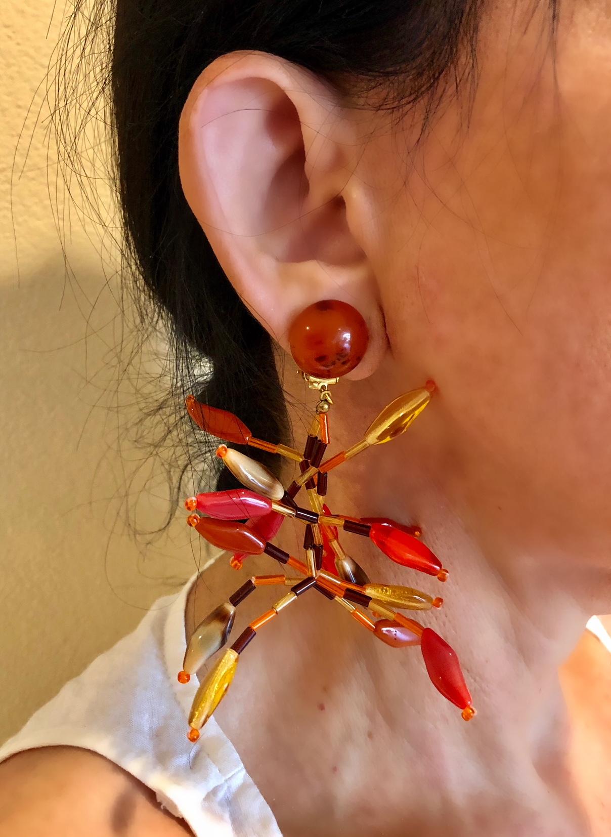 This unique handcrafted pair of chandelier clip-on earrings has a definite wow factor, comprised of a plethora of German glass beads in hues of orange, brown and yellow and are accented by a large bakelite domed button on top. The earrings