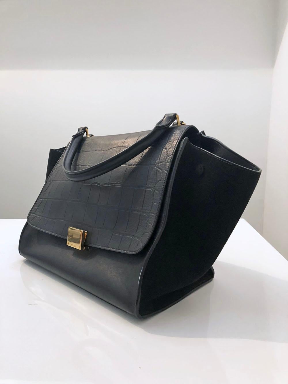 Celine Black Trapeze Medium Size Bag with Embossed Crocodile Flap.

Celine Trapeze Medium in black with embossed croc top flap and suede wings. Features a detachable shoulder strap. One external zipper pocket on the back and two internal slide