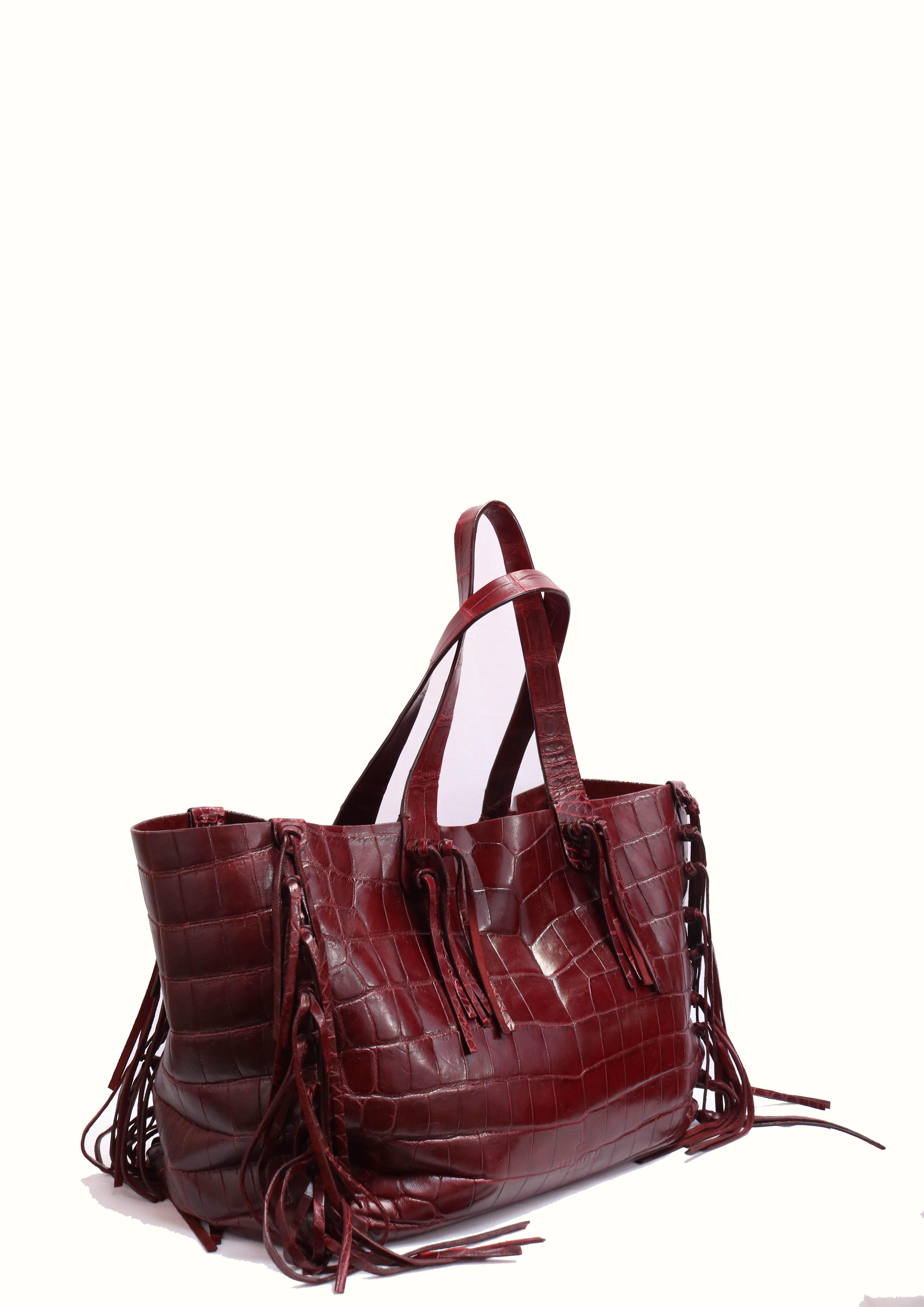 Crocodile leather tote bag in red with fringe trim, and open top. 
-Suede interior with patch and zipper pockets 
-Red wine tone 
-Made in Italy.