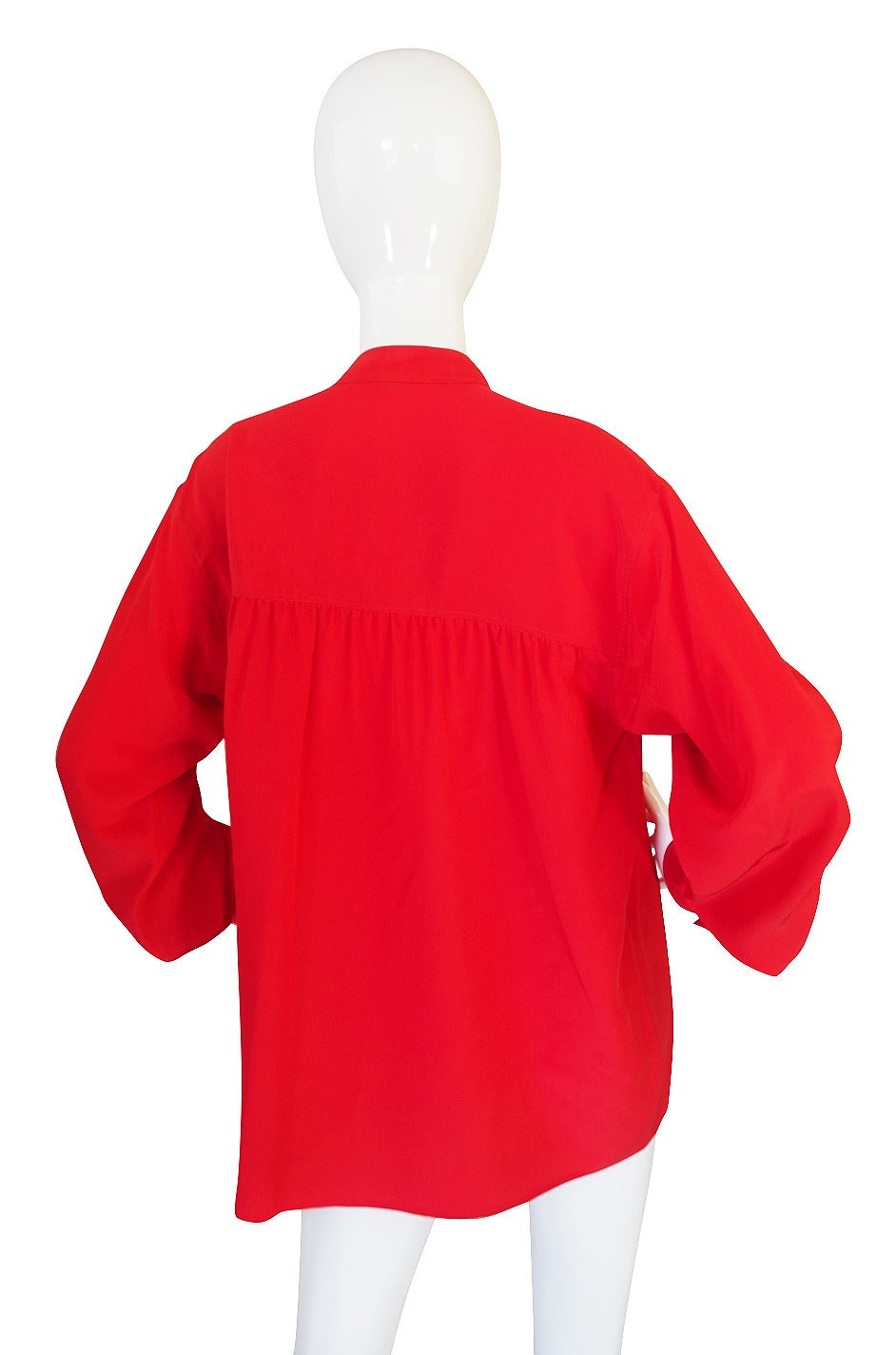 Classic silk blouse from Yves Saint Laurent that is done in a beautiful red silk! It has that classic YSL feel with a great smocking detail in the way the silk is set under the shoulder panel. I love the simple neckline with its neat little collar -