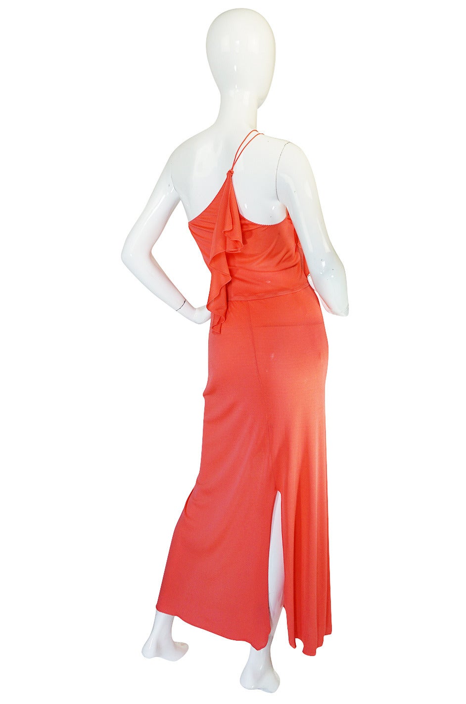 An amazing slinky and fluid jersey sheath in a bight coral jersey that skims over the body and is cut to emphasize every curve. It is long and lean with a trailing ruffled detail that gives it lots of movement. The dress is cut on the bias so it