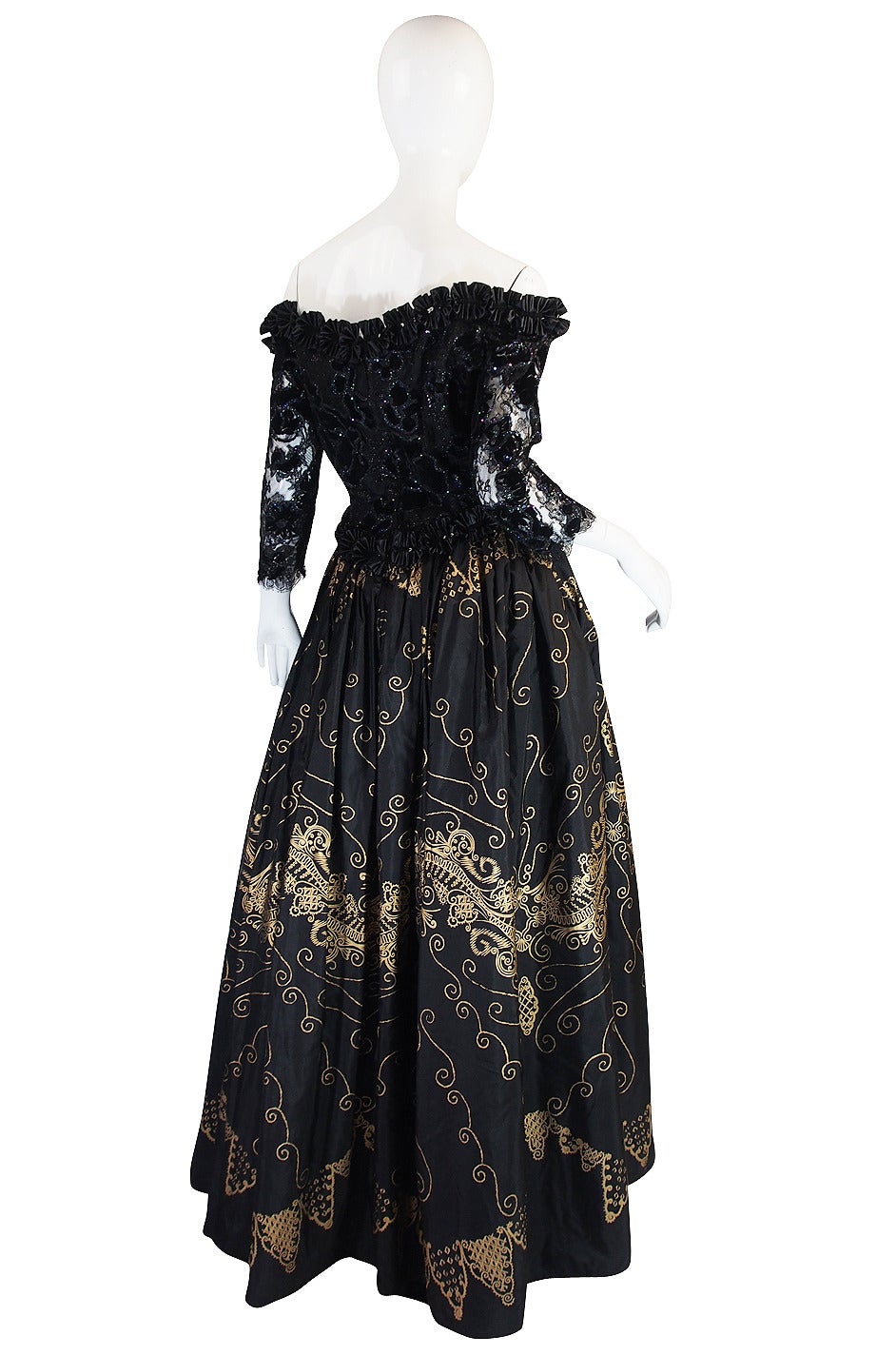 This stunning and dramatic black and gold, hand painted gown by Zandra Rhodes is deliciously decadent in every way. The bodice is made of a  silk with a velvet fused floral pattern highlighted with glitter. The sleeves take this a step further with