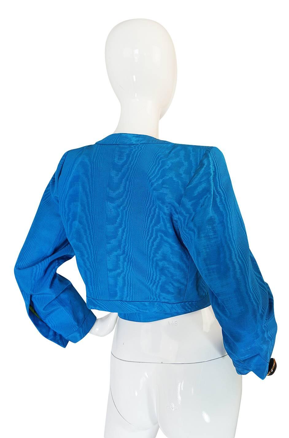 What a great little Yves Saint Laurent jacket. It is the perfect pop of color and it even has a matching belt with it that makes it so versatile. It is made of a rich silk moire fabric in a beautiful shade of blue. The inside is also finished in