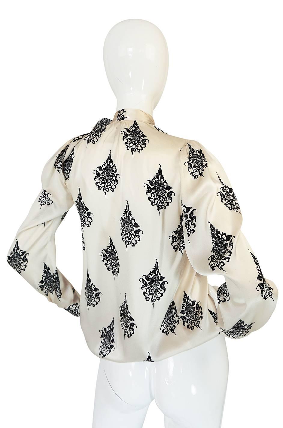 This Yves Saint Laurent silk top is a beauty. The cut is loose and easy and the fabric a very fine silk with a satin finish in a beautiful cream with a black print over its surface. Each sleeve is cut to puff slightly above the button cuffs. The