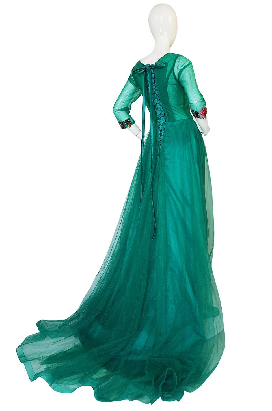 This is most likely a more modern piece but has a lovely vintage feel to it. The combination of colors used on it and its sweeping lines and train make it appropriate for the grandest of events. The body of the dress is made of a emerald green net