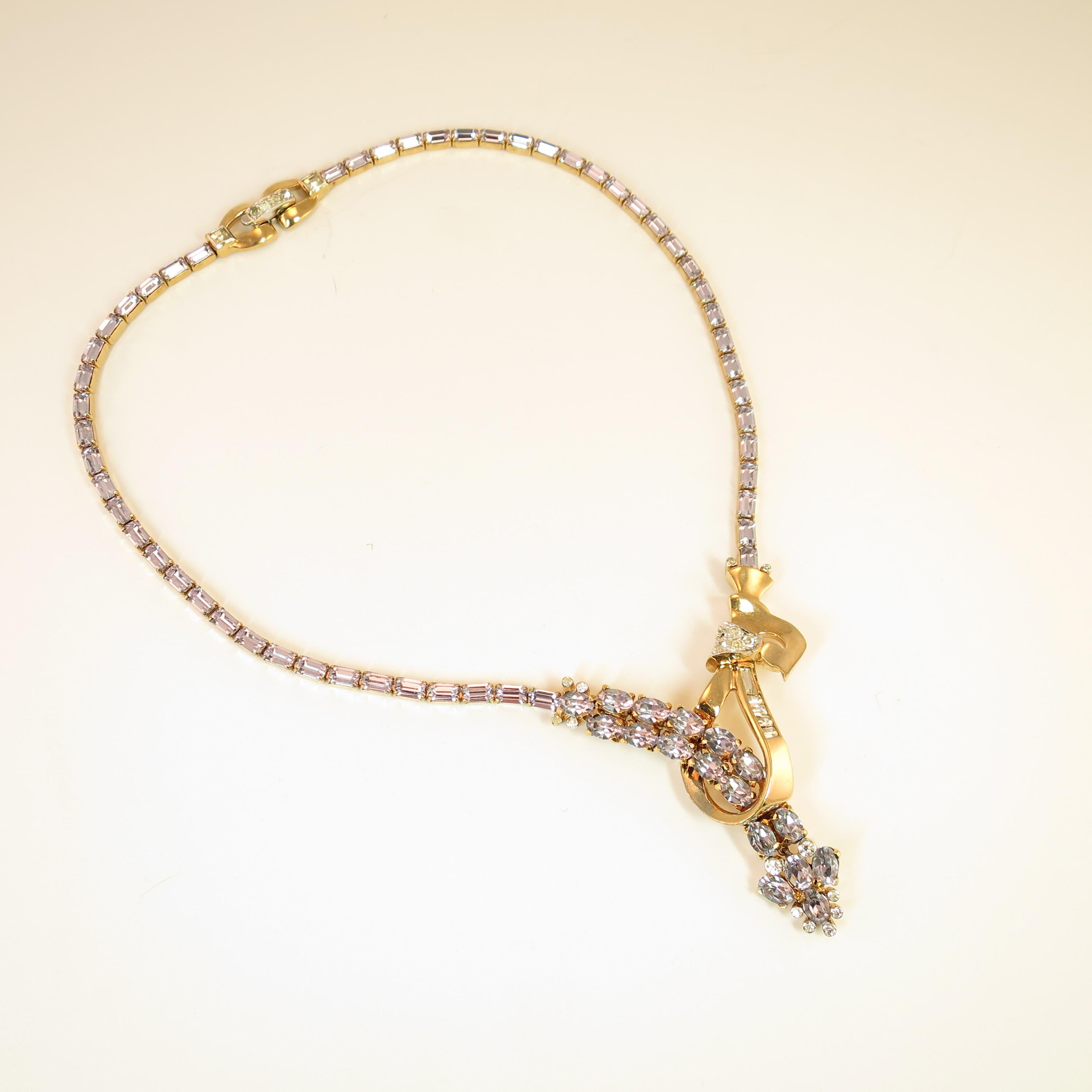 Offered here is a Mazer Bros. gold-plated rhodium necklace and matching clip-back earrings from the early 1940s. The necklace reveals an asymmetrical looped ribbon and arrow design with an articulated dangle; it features color-change alexandrite