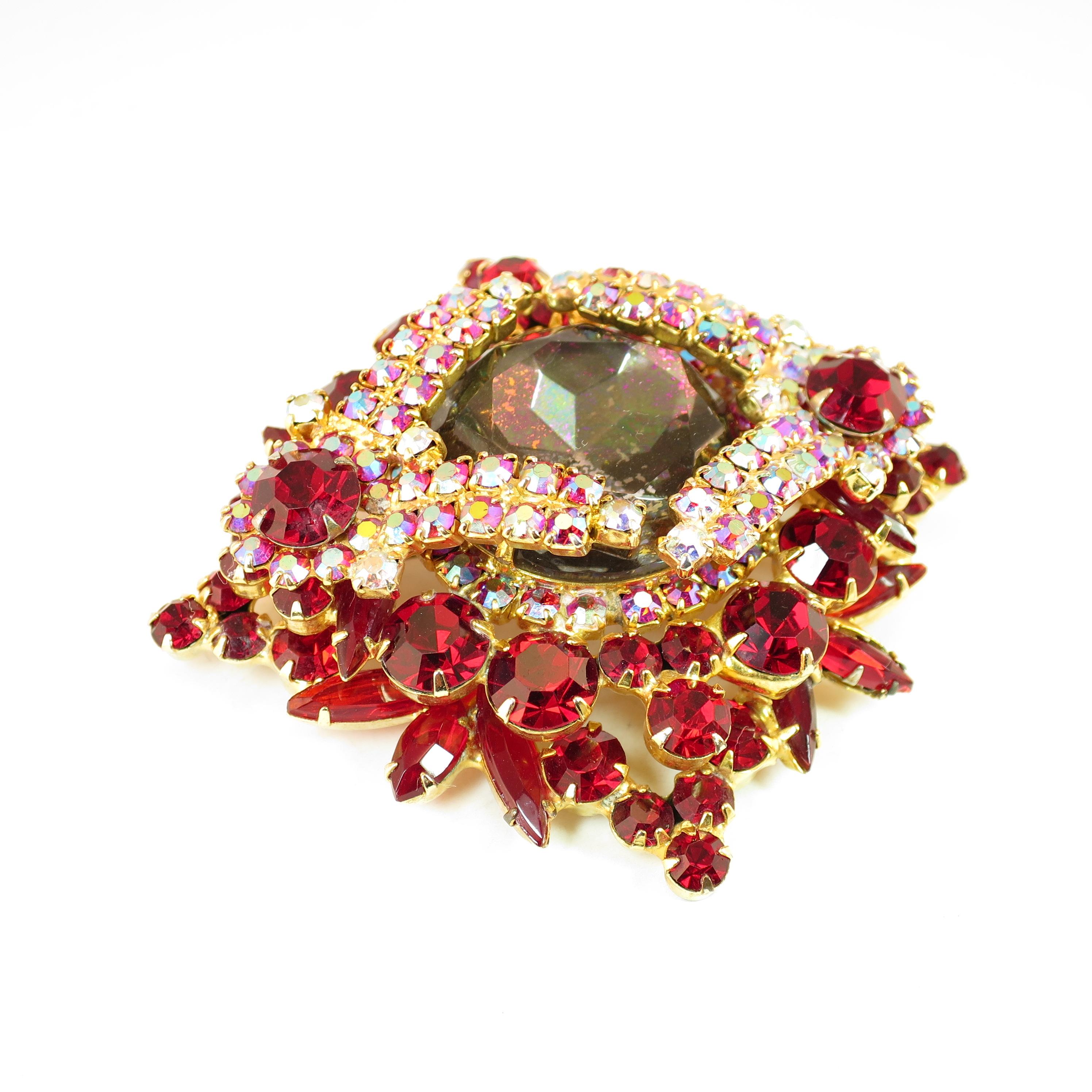 Offered here is a DeLizza & Elster Juliana massive gold-plated brooch from the 1960s. A tiered three-dimensional design is focused on a huge faceted gray-smoke center stone atop several layers of garnet crystals in marquise, navette, & round cuts.