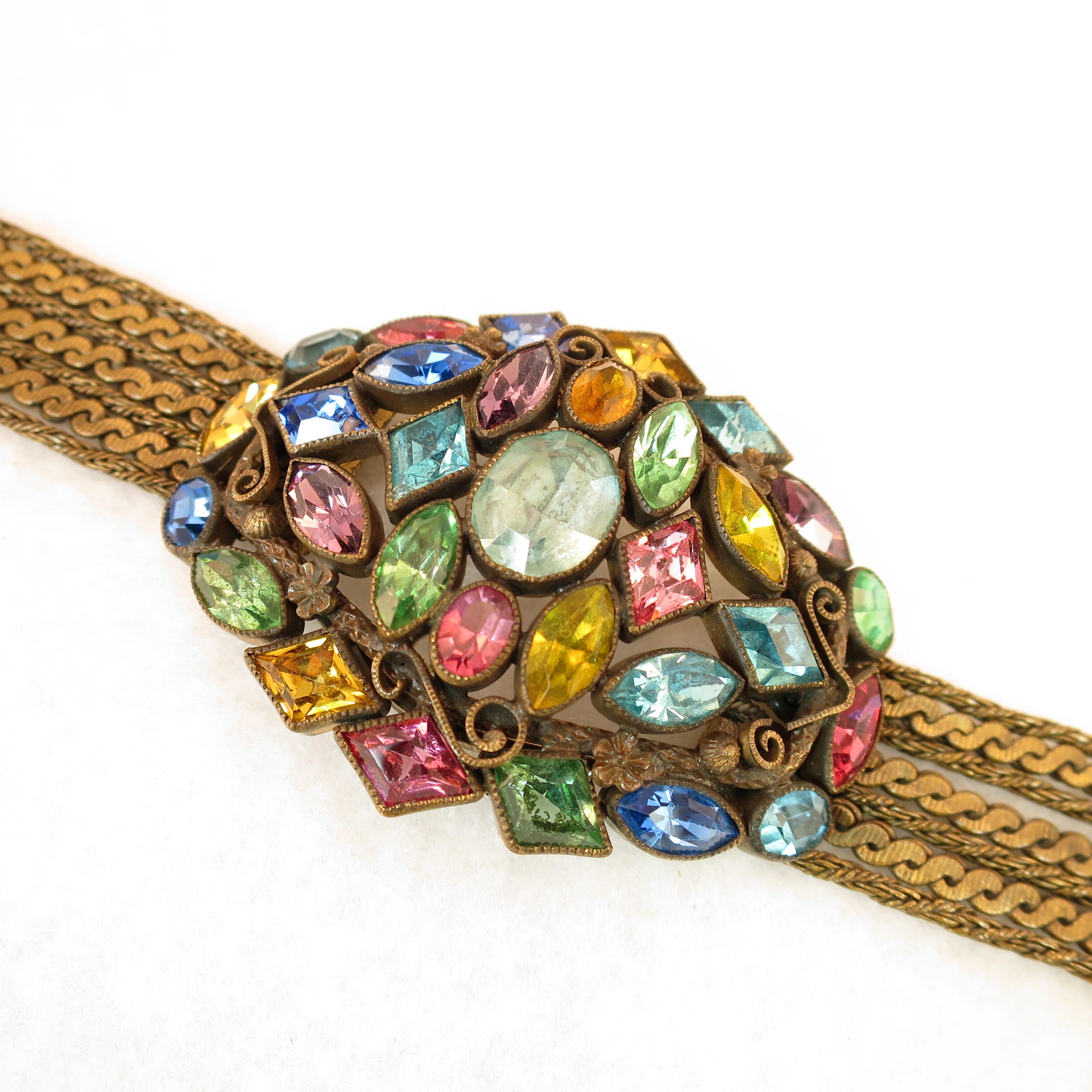 Offered here is a Czech Art Deco gold-washed bracelet with jewel-tone Bohemian crystals and chains from the 1920s. The massive centerpiece in a domed stacked open-work design is embellished with tiny rosettes and curls, and presents