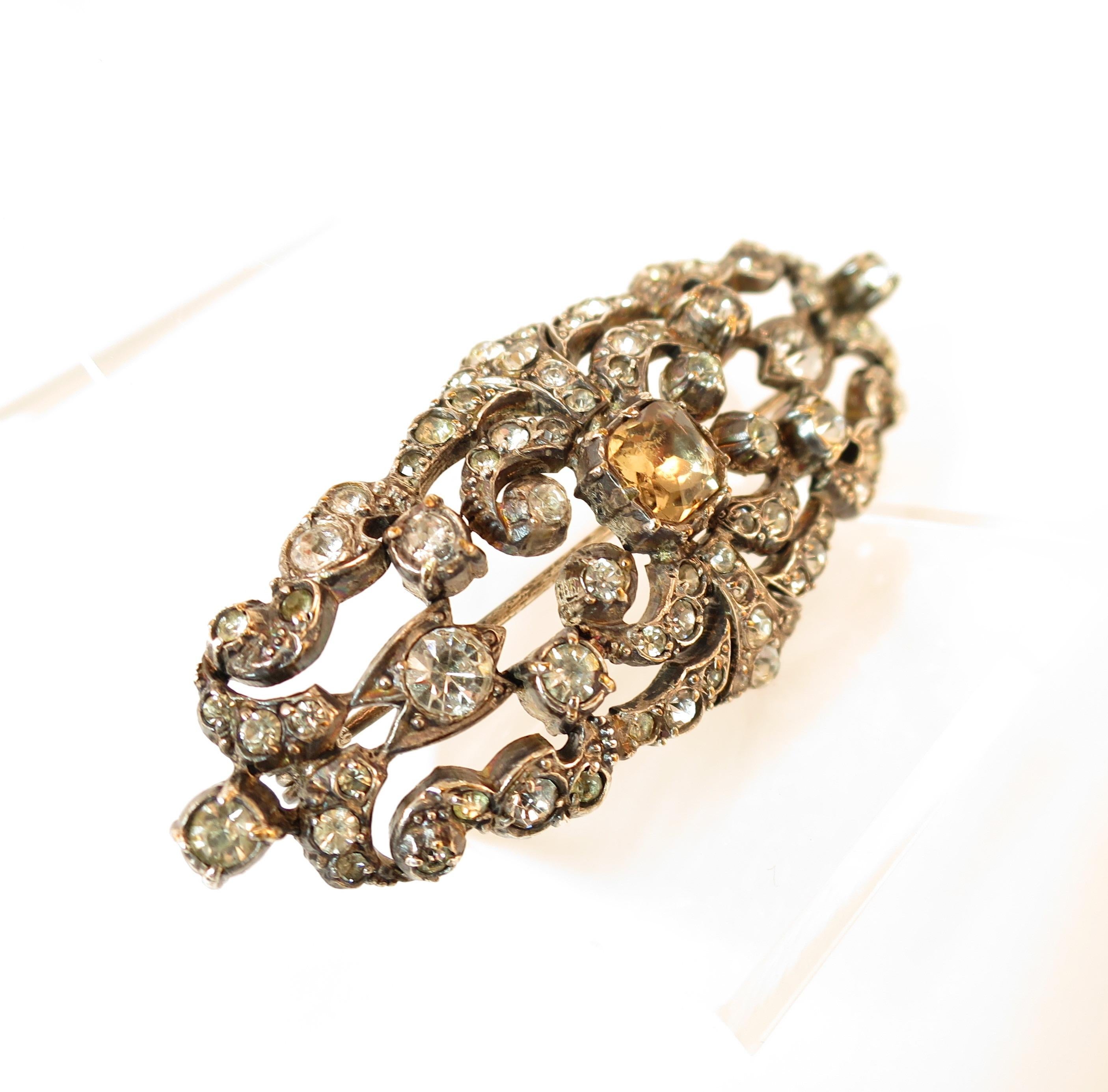 Offered here is an Edwardian hand-fashioned sterling silver brooch set with French paste stones, Circa 1905. Within the elongated oval and slightly domed shape of the brooch, there is an elaborate curving foliate cut-work design; it is embellished