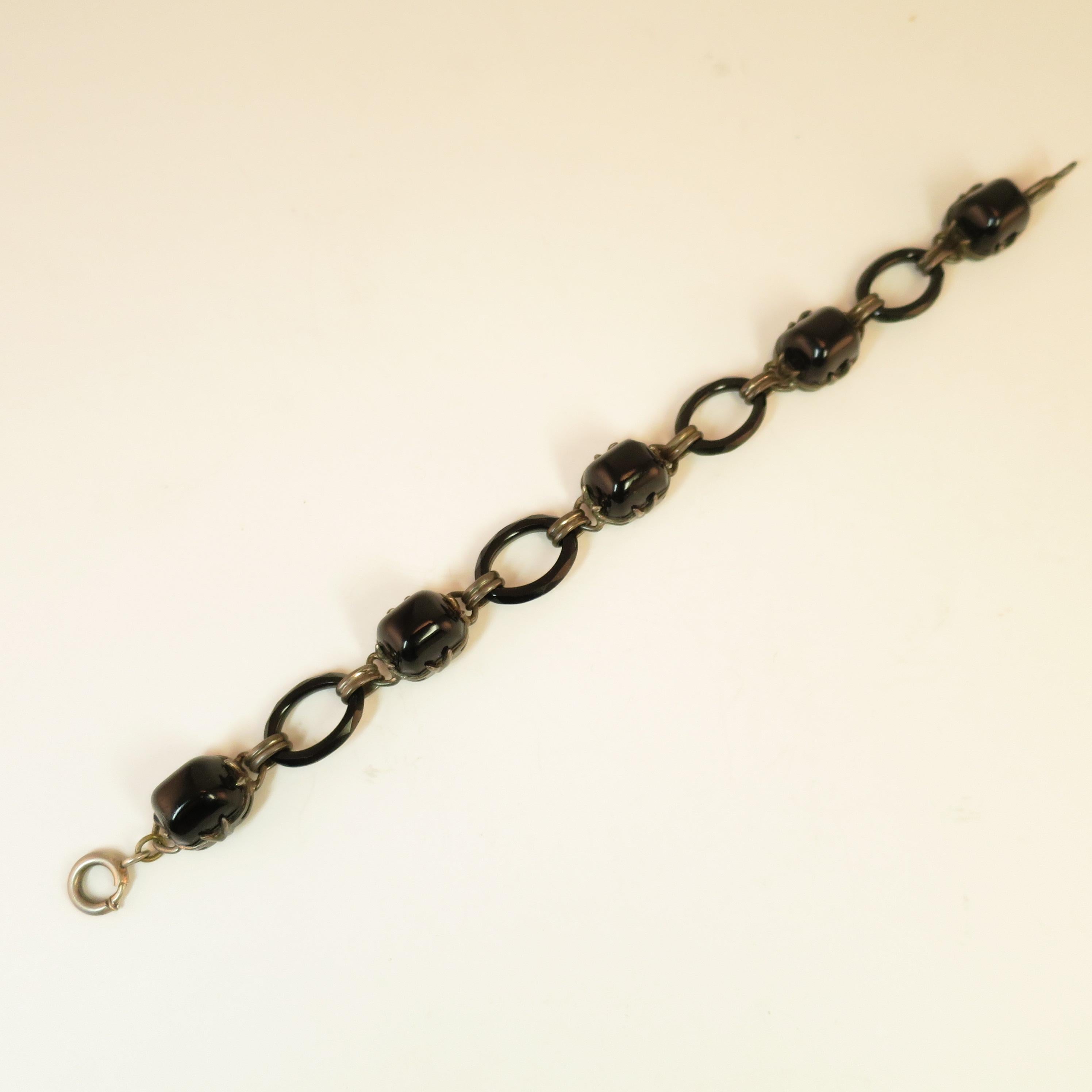 Offered here is an Arts & Crafts sterling silver & French jet link bracelet, Circa 1900. Sugarloaf cabochons of intense black French jet glass in open-back claw-prong settings alternate with oval rings of faceted glass, linked by flattened ribbed