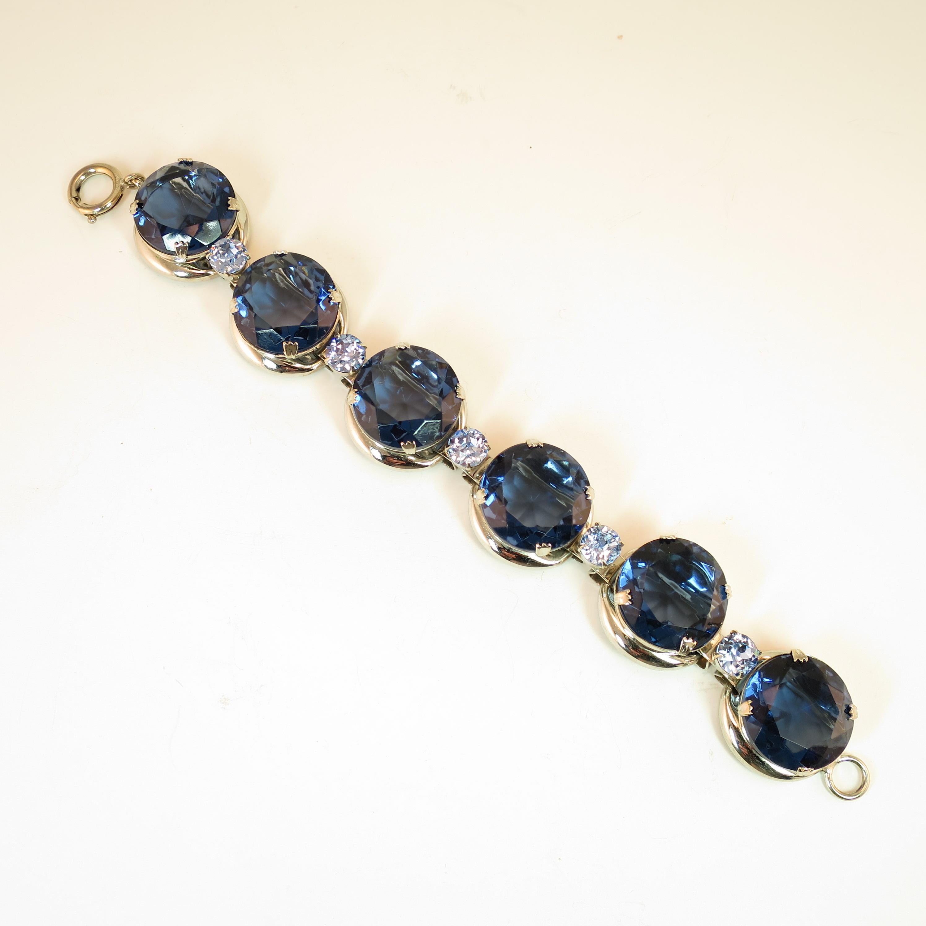 Offered here is a massive German silver-plated link bracelet featuring sapphire headlamp crystals, from the 1950s. Round stations have a base platform with a rectangular opening underneath a deep cup setting, allowing light to shine through the