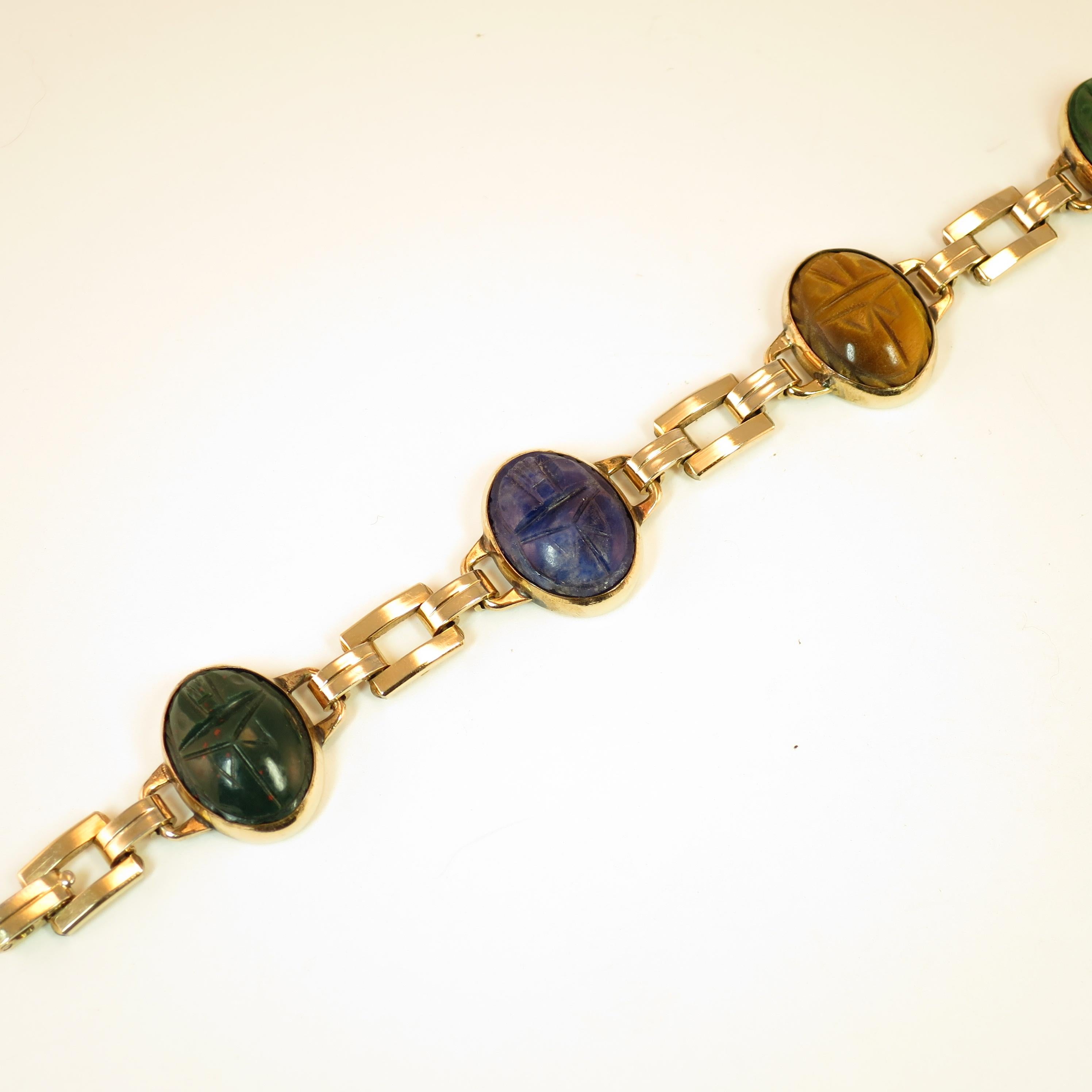 Offered here is an Art Deco Egyptian Revival 10k gold-filled over sterling silver link bracelet by the Engel Brothers of New York, from the 1930s. Open rectangular links alternate with open-back bezel-set oval carved scarabs of semi-precious stones