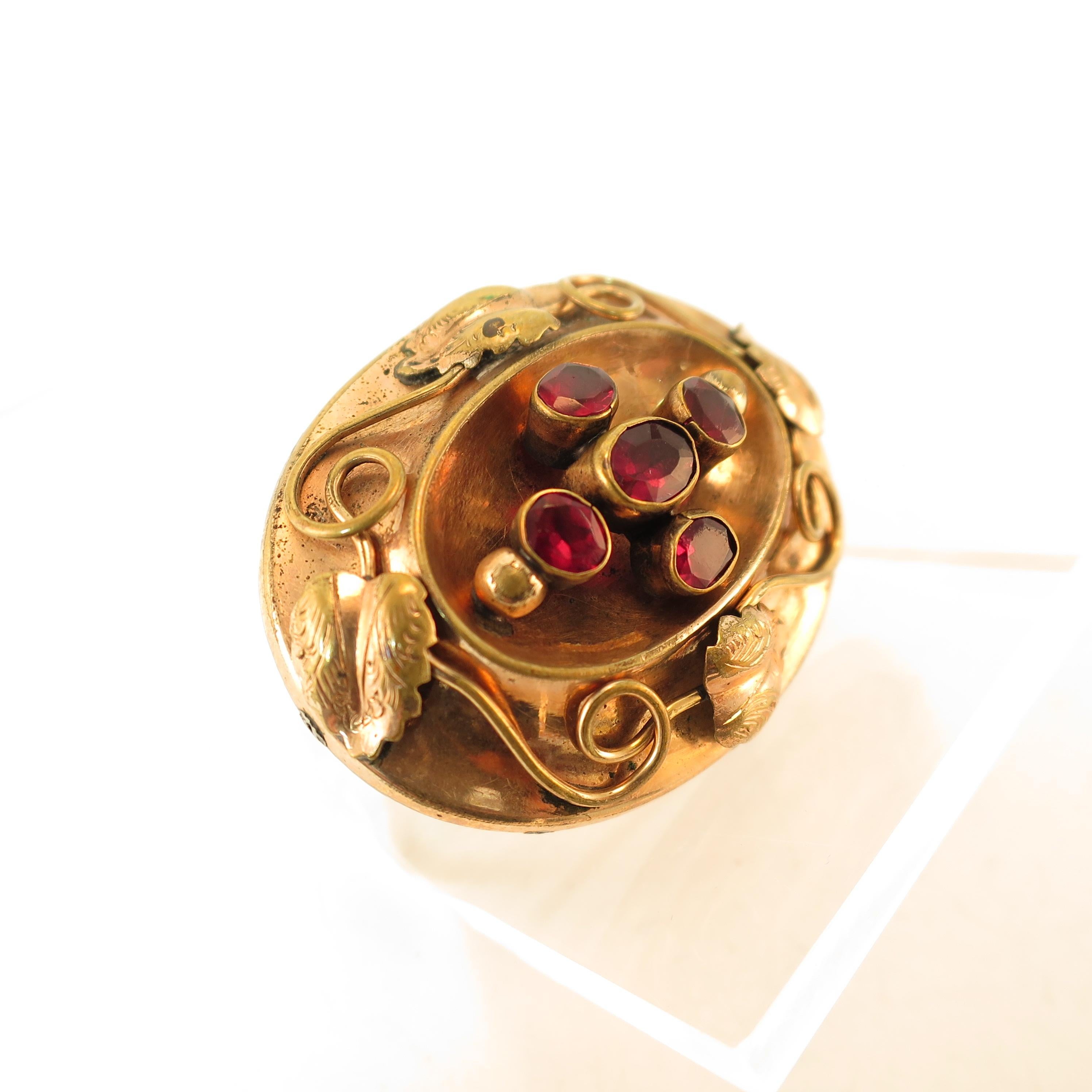 Offered here is a Victorian 10k gold hollow-ware brooch with garnets from the 1860s. The oval curved hollow-ware platform is centered with a shadowbox design within which are five faceted garnets in tall collet settings -- a slightly larger center