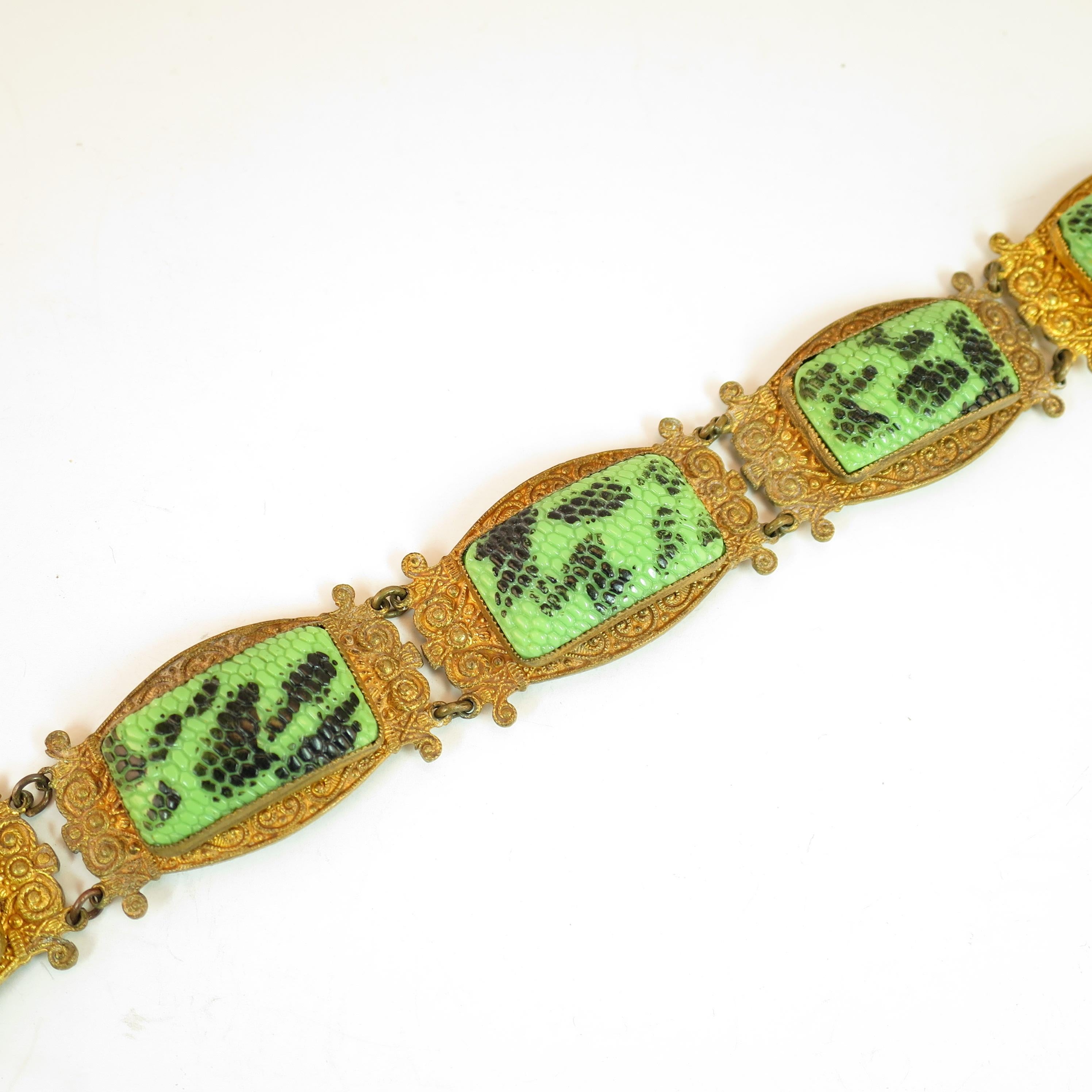 Offered here is an Art Deco Czech Egyptian Revival snakeskin glass bracelet from the 1920s. Five gold-washed slightly-curved panels are embellished with cannetille filigree in elaborate curling designs. Atop these platforms in serrated bezel