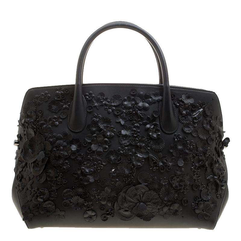 A refreshing twist to a classic black bag, this Dior bag is every bit drool-worthy. Crafted from a black leather body, this bag features floral applique all over and comes fitted with two rolled top handles. Decorated with 'Dior' charms, this bag