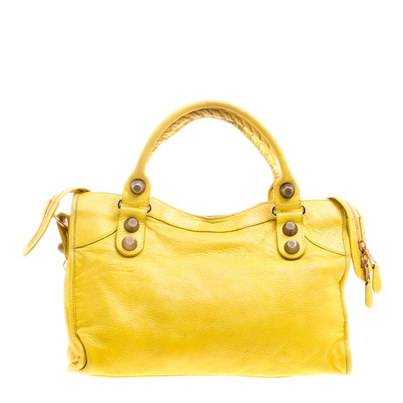 This Classic City GSH tote from Balenciaga is perfect for all your outings. This yellow leather bag is unique in its silhouette and features an interplay of large studs and buckles. With a creative edge, the bag has a front zip pocket, round leather