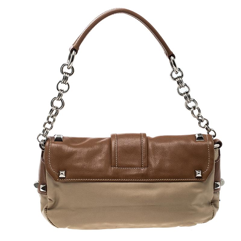 Classy and popular is what you can call this shoulder bag that comes in beige and tan. Made by the finest, this Prada creation lives up to its reputation. It has been crafted from nylon and leather and designed with a single handle and stud