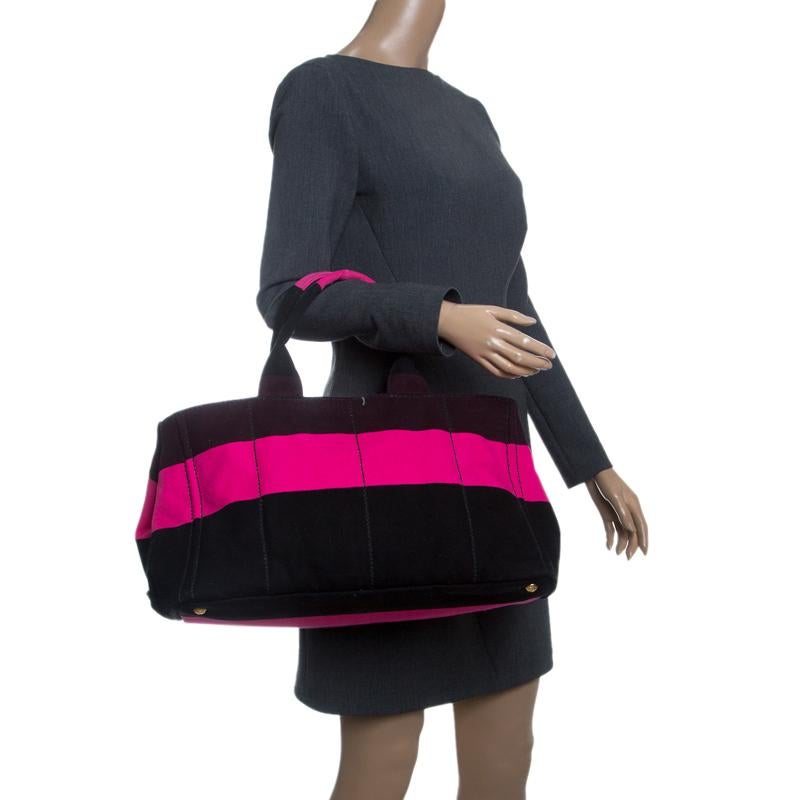 Finely crafted with pink and black striped canvas, this tote from Prada features canvas top handles and protective metal feet at the base. The open top leads to a canvas-lined interior that comes equipped with a zipper pocket. This lovely creation